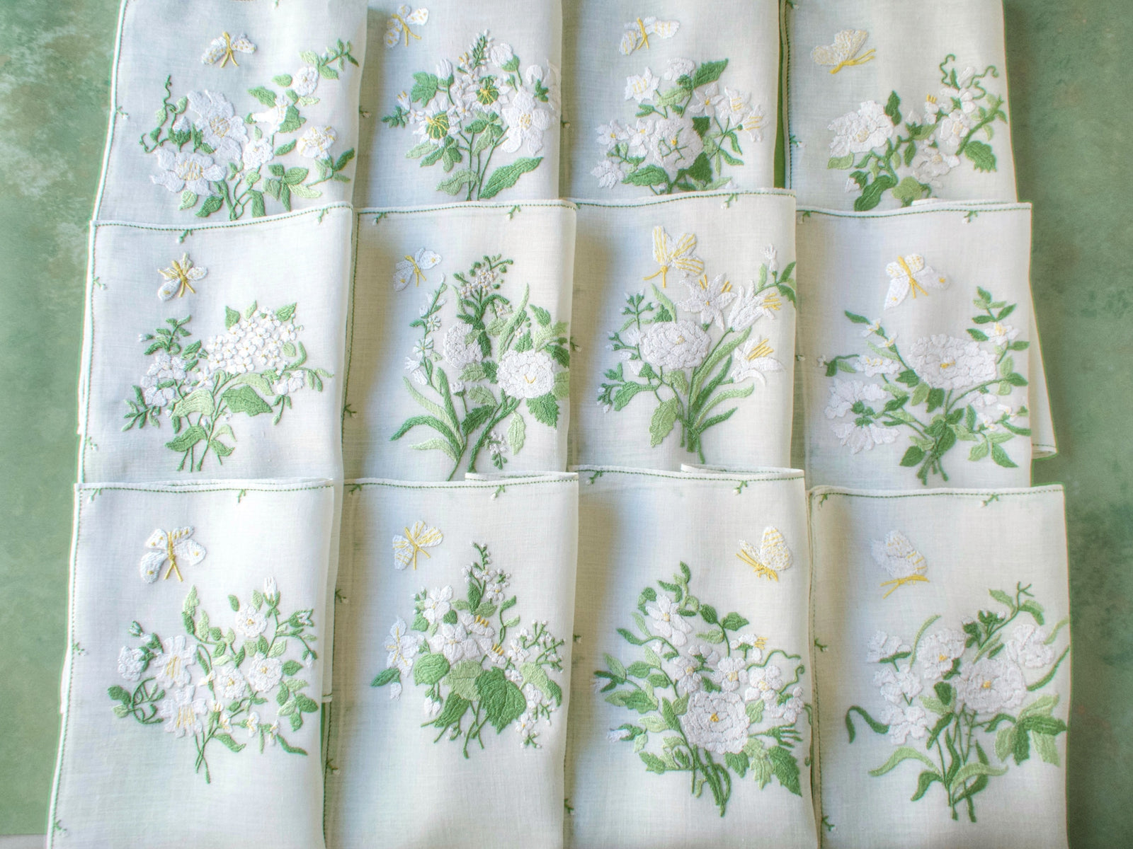 Row of folded Rapisardi placemats showing varied white floral bouquets and individual butterfly placement.