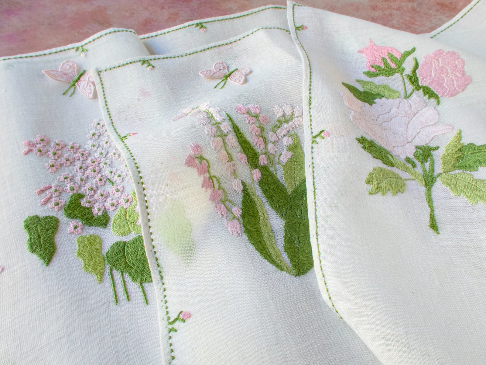 Pink Rapisardi placemats with trembler butterflies, each featuring a different embroidered flower on semi-sheer linen.