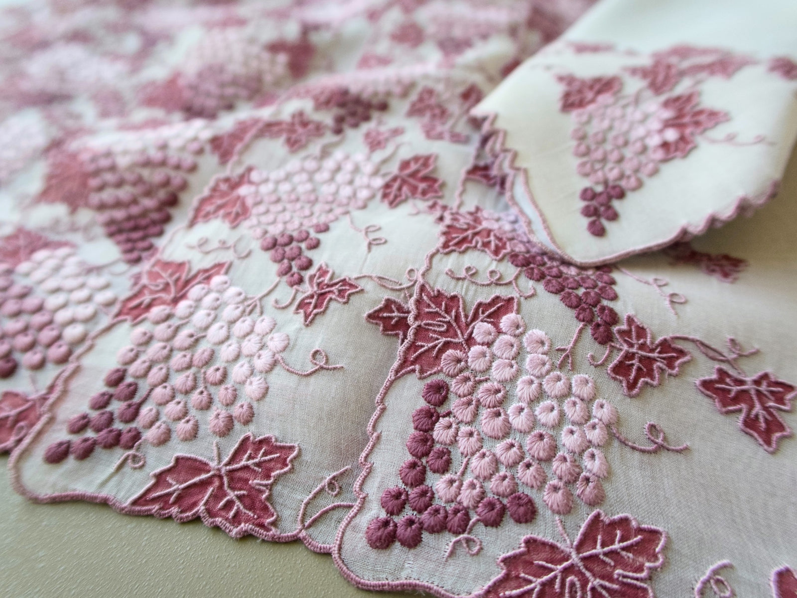 Close view of a vintage Marghab Vineyard placemat with hand embroidered pink and burgundy grape clusters and organdy appliqué leaves