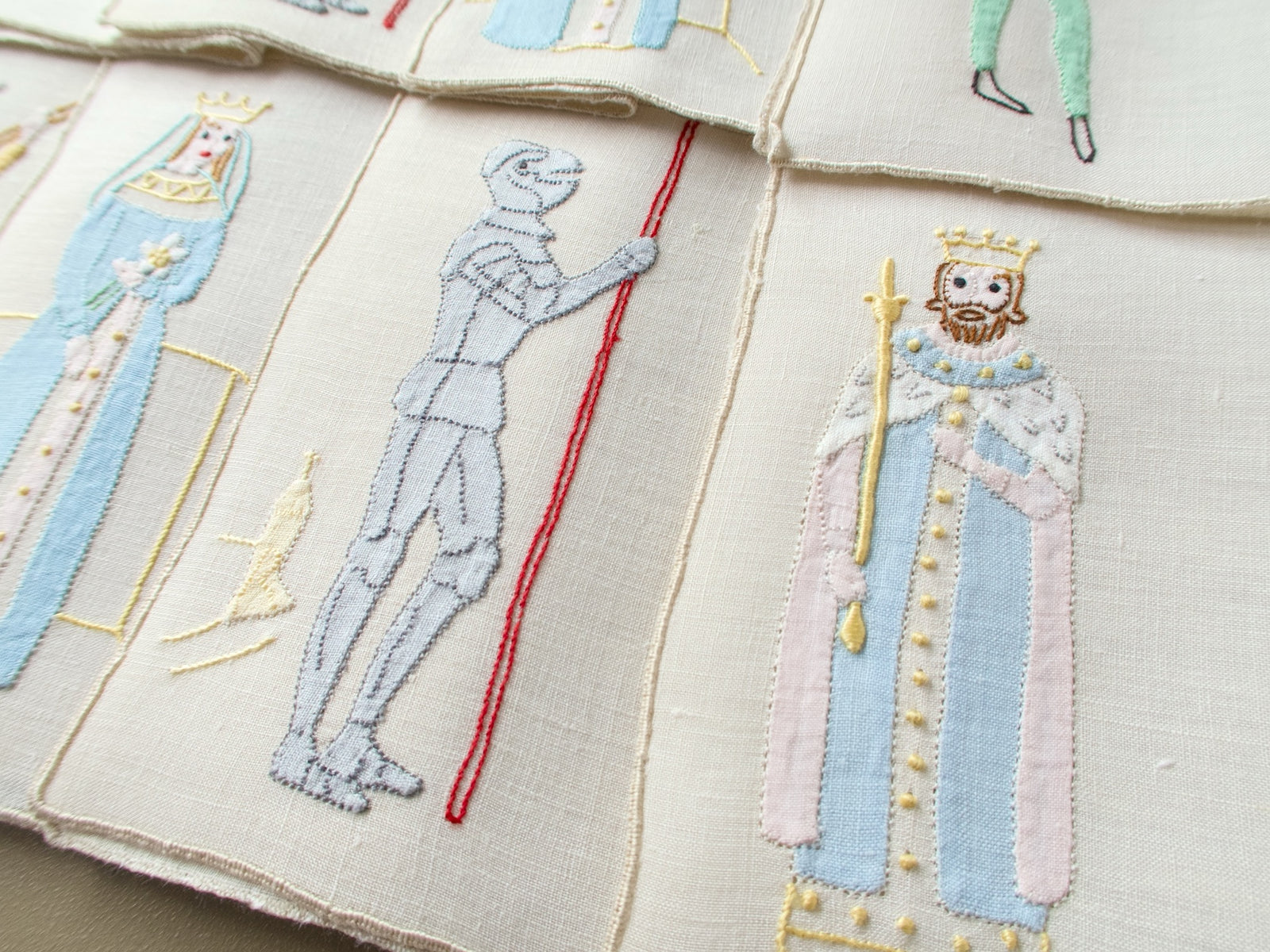 Close view of vintage Madeira cocktail napkins with an appliqué queen, jack in armor and king on linen