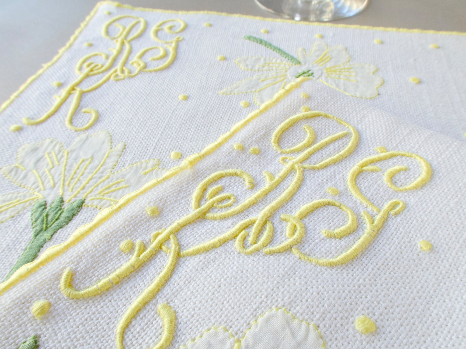 Close-up of elaborate cursive yellow monogram hand embroidered in Madeira on white textured linen