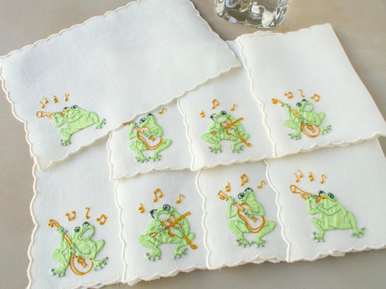 Stack of vintage Madeira hand embroidered linen cocktail napkins showing dimensional musical frog embroidery and scalloped edges