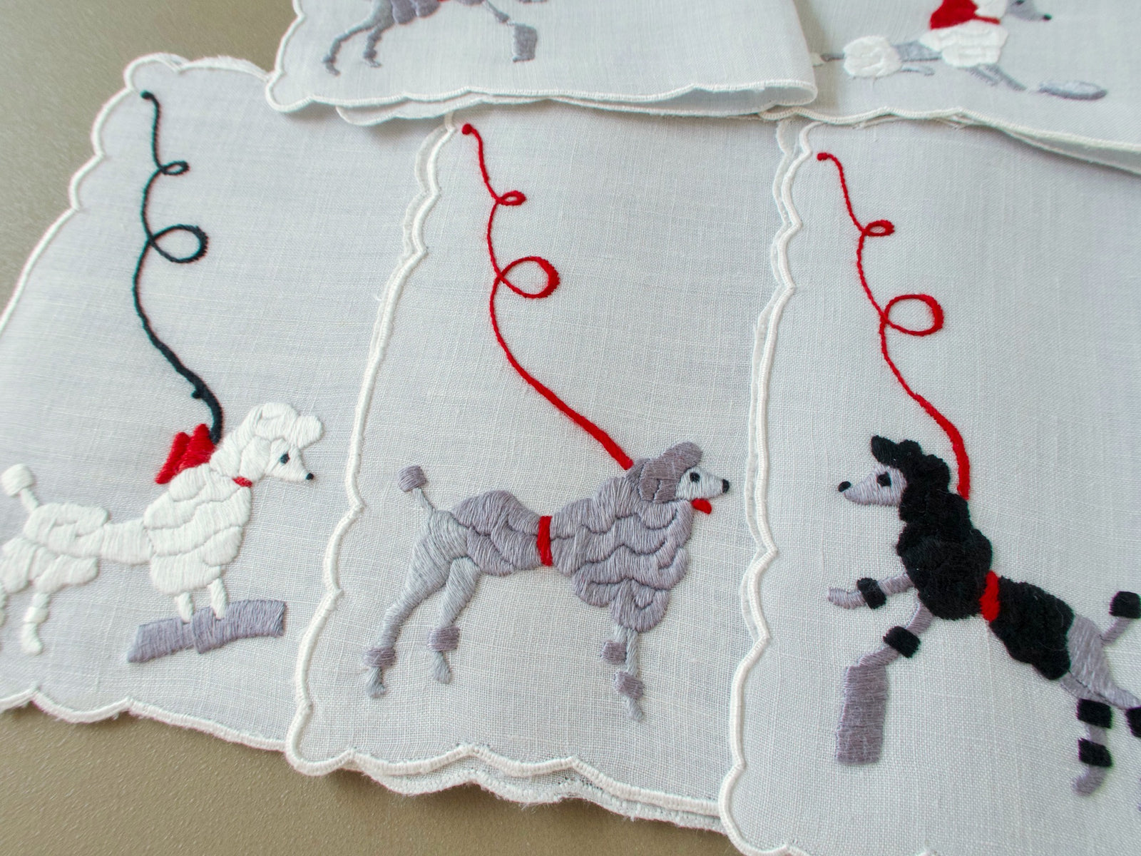 Three vintage Madeira cocktail napkins with a white poodle in a red bow, a gray poodle and a black poodle, each on a looping leash
