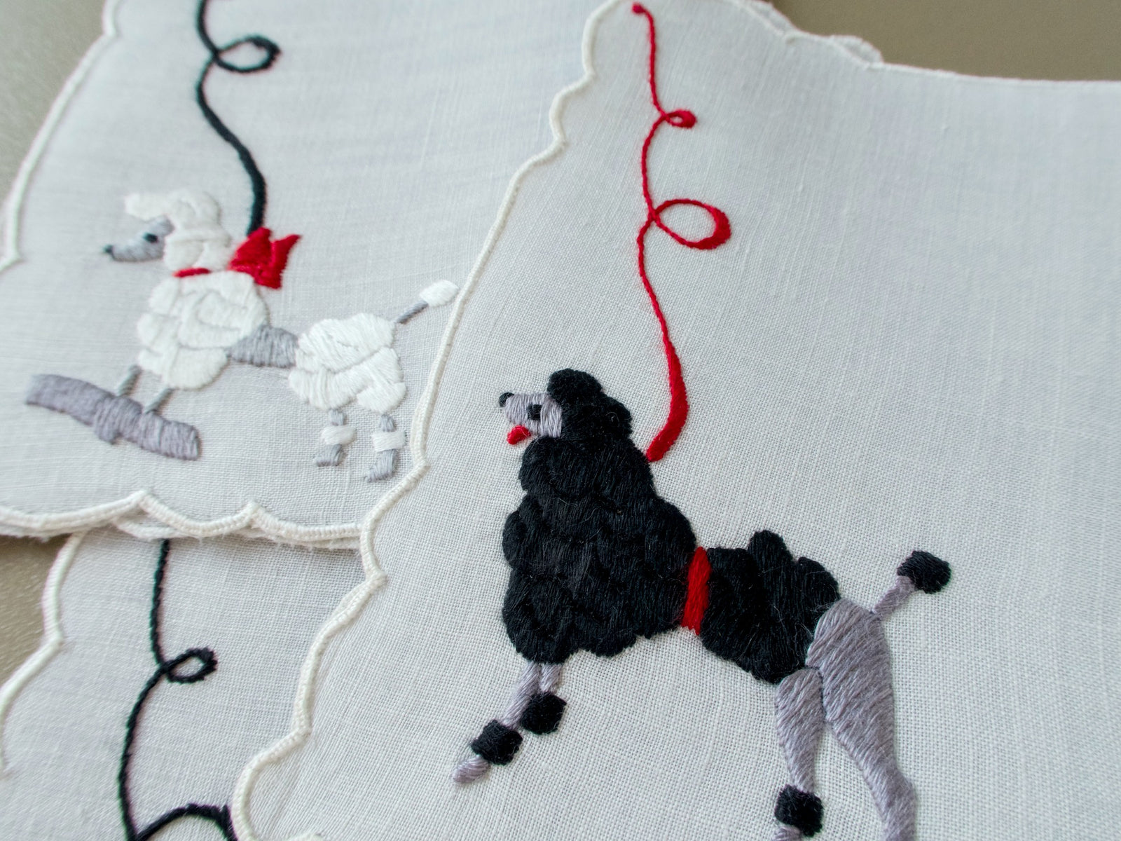 Close view of a black poodle with a red collar beside a white poodle perched on a block