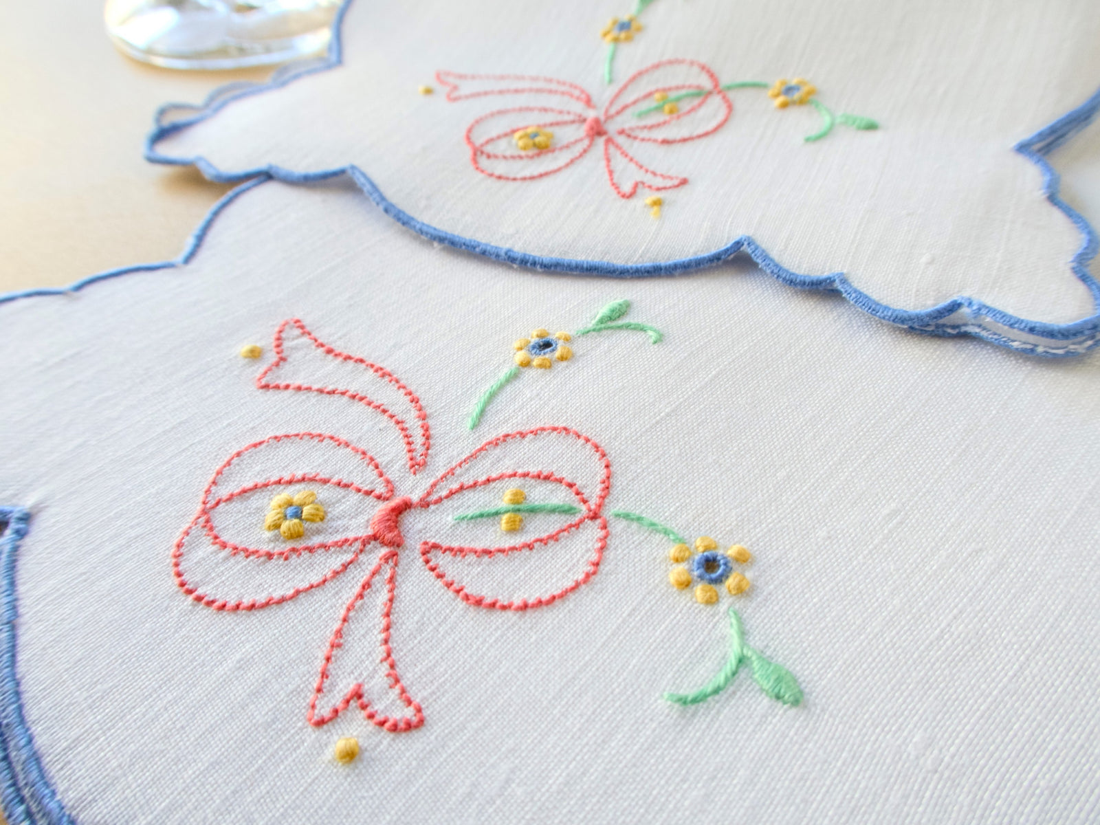Closeup of vintage Madeira linen cocktail napkins hand embroidered with pink ribbon bows and scattered yellow and blue posies