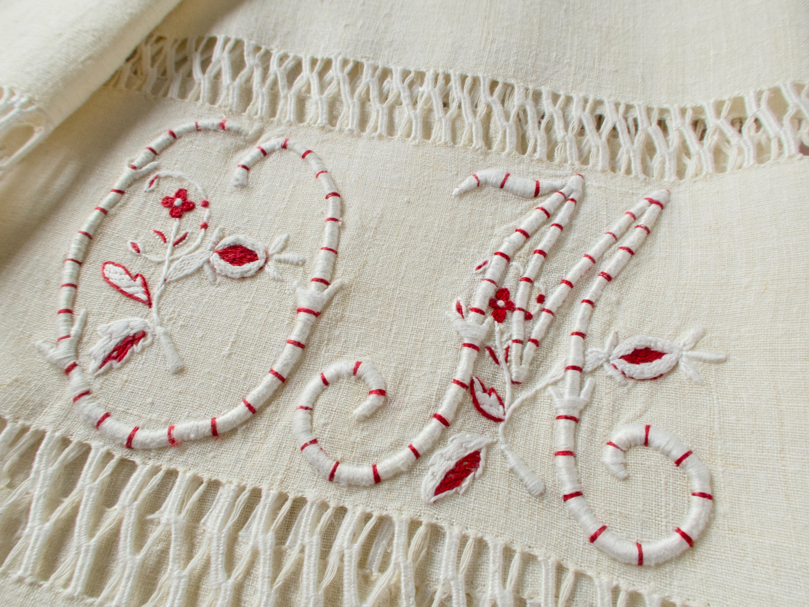Detail of individual letters of hand embroidered “OM” monogram on vintage French homespun linen, showing padded satin stitch technique and red detailing