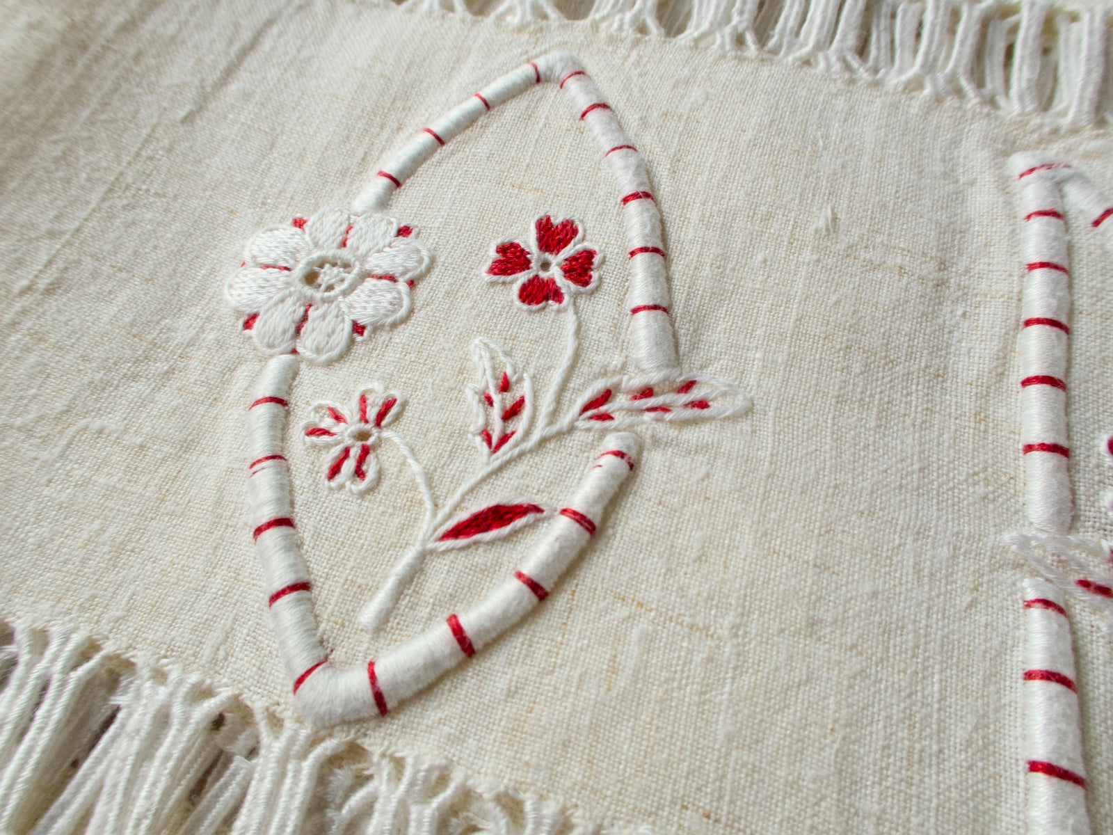 Detail of vintage French linen towel showing hand embroidered floral accent and red detailing alongside knotted fringe edge