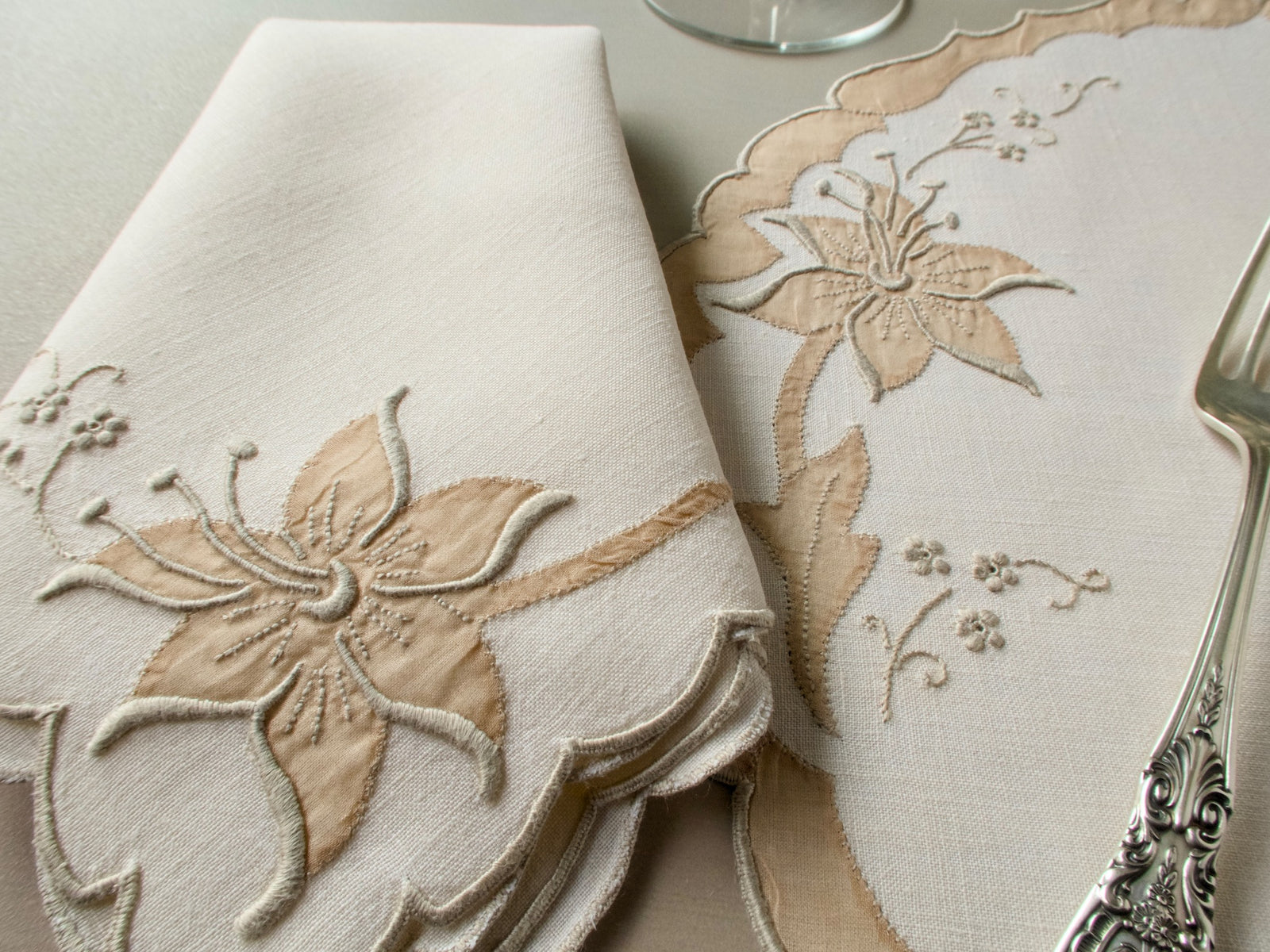 Close-up of vintage Madeira placemat and folded napkin showing richly dimensional lily in organdy appliqué on ecru linen with scalloped organdy appliqué border