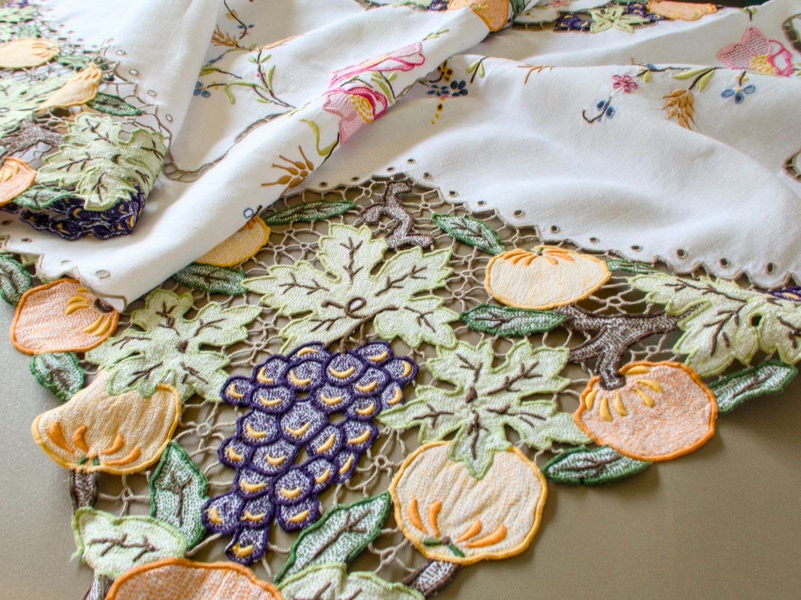 Corner of a vintage Madeira linen tablecloth with hand embroidered pumpkins, grapes and vine leaves in Richelieu cutwork