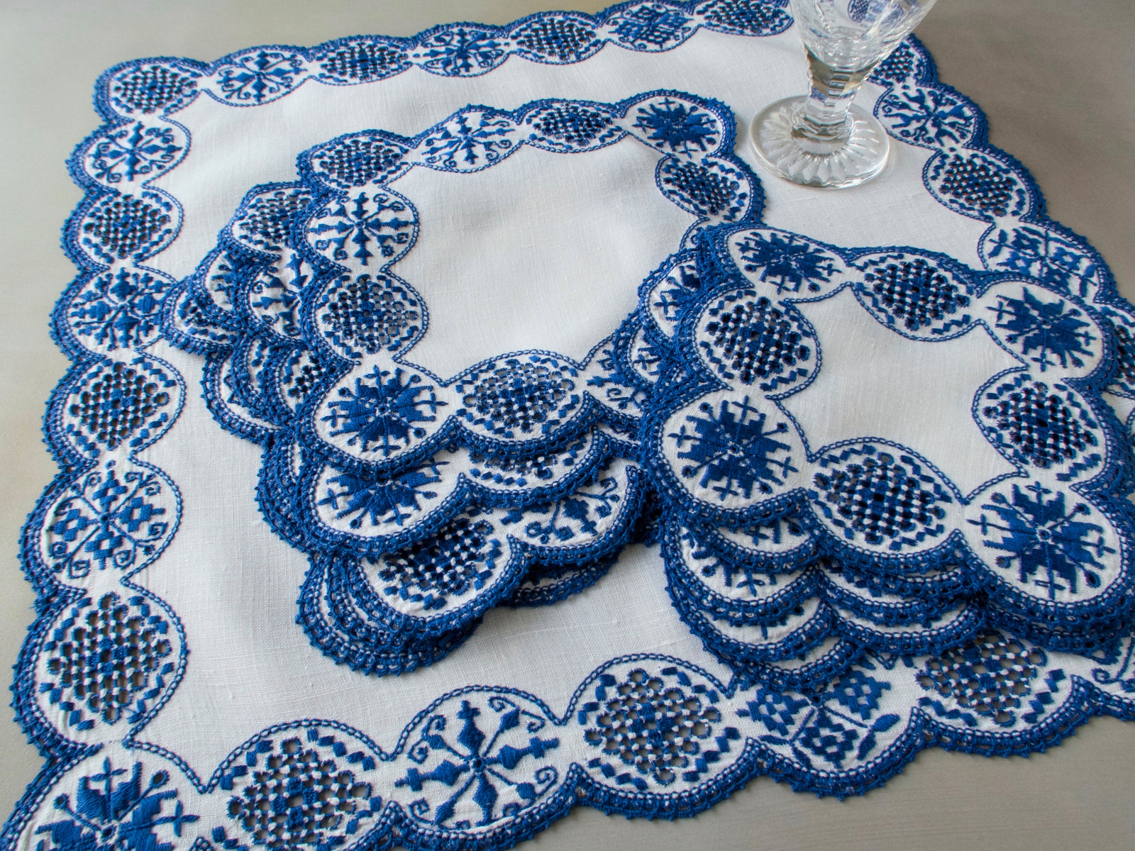 Overhead view of vintage Italian white linen centerpiece with cobalt blue geometric embroidery and scalloped edges