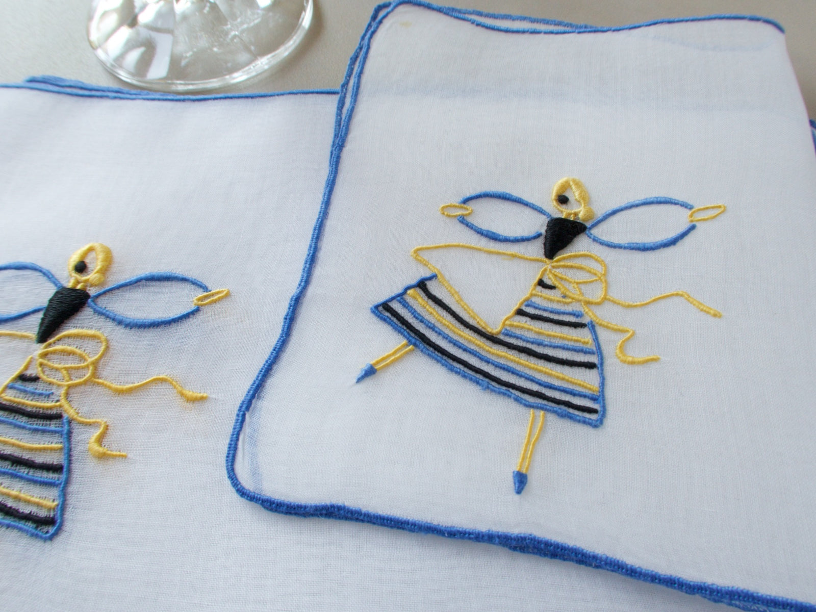 Marghab Dancer cocktail napkins, hand embroidered in yellow, blue, and black on sheer white organdy.