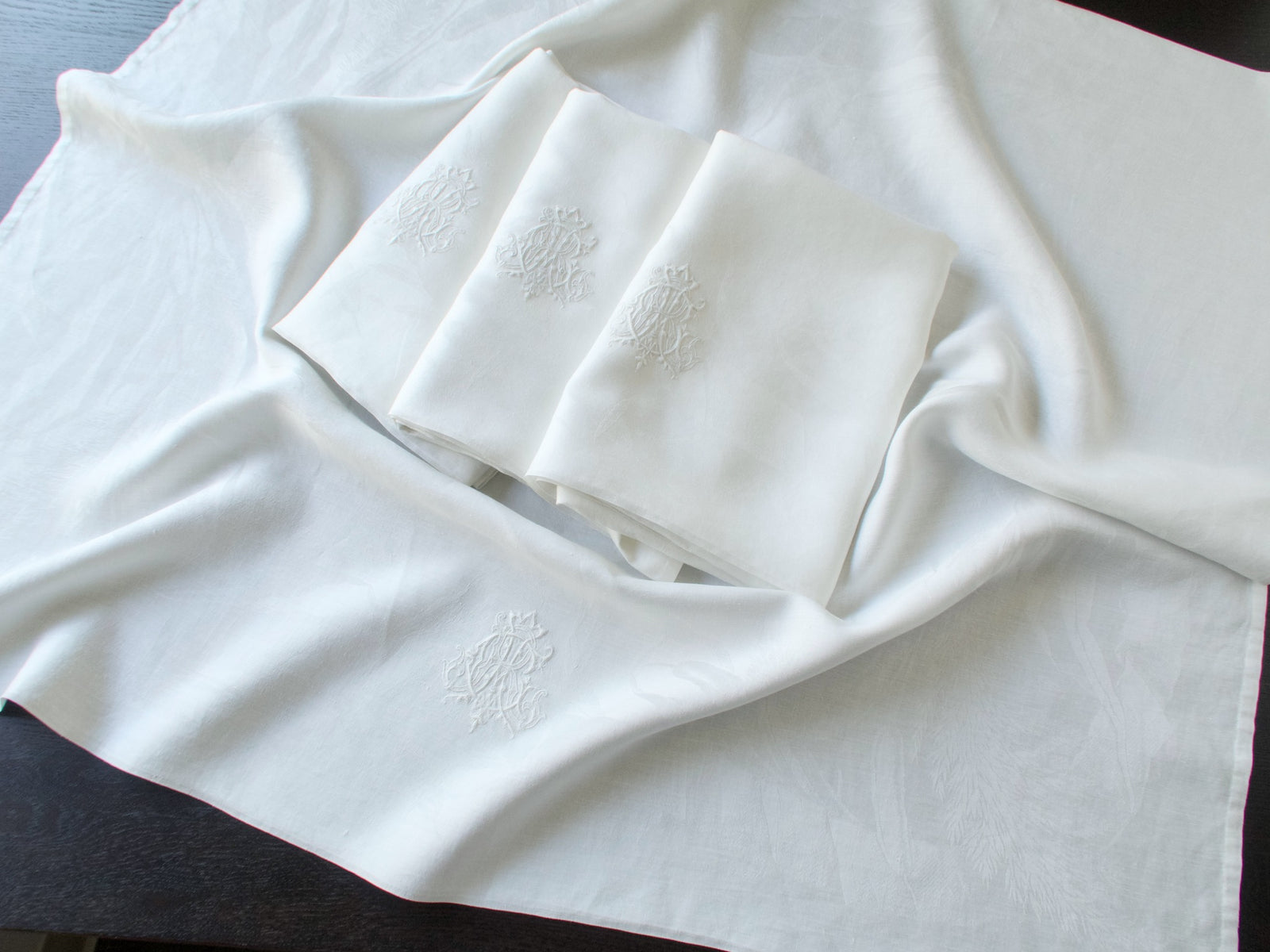 Antique damask linen napkins folded and stacked, one embroidered ACR monogram catching the light