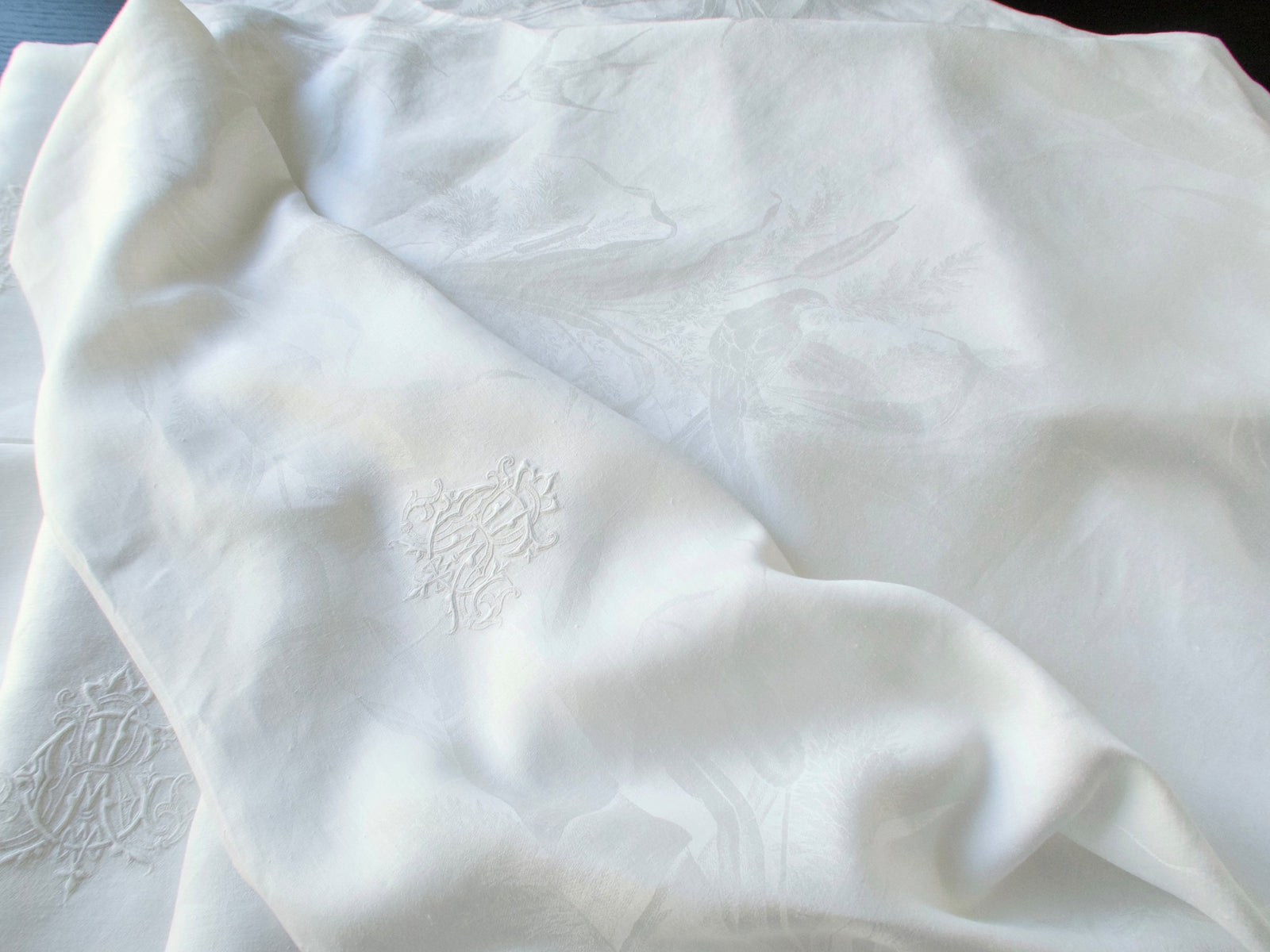 Close view of an antique damask linen napkin showing the woven bird and reed pattern beside the embroidered ACR monogram