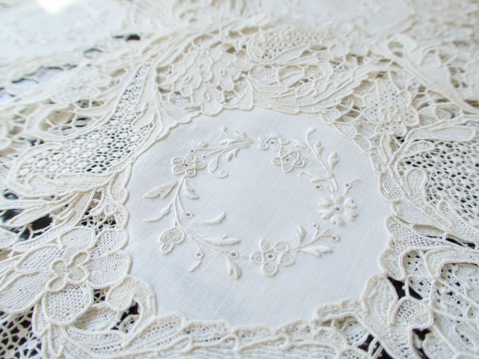 Close view of the hand embroidered floral wreath at the center of an antique linen placemat