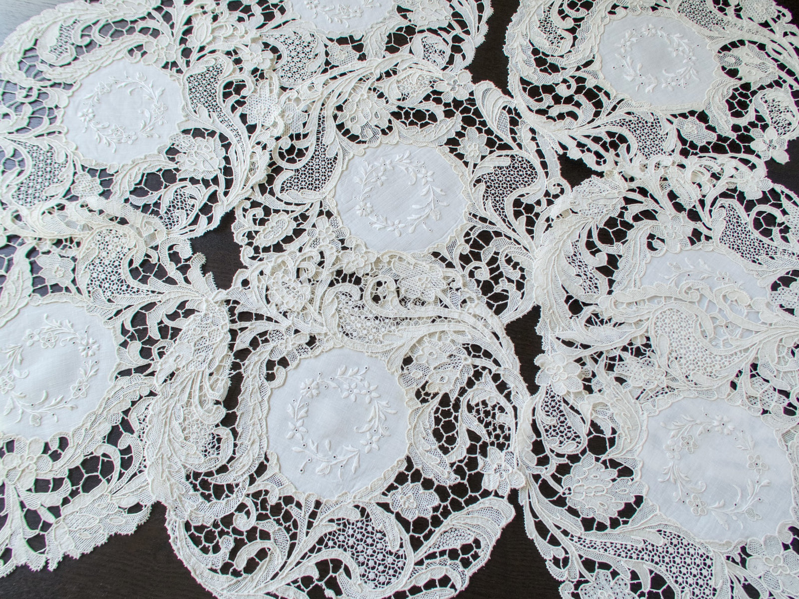 All eight antique Point de Venise lace placemats arranged together showing the embroidered centers and lace borders