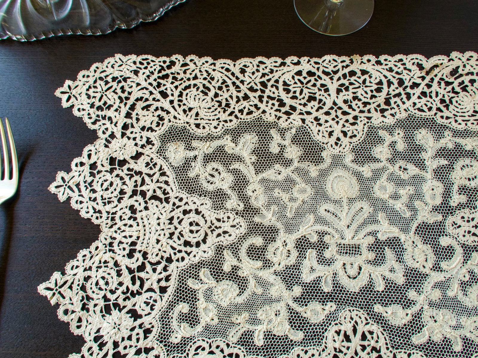 Antique lace placemat with pointed bobbin lace sides and a Milanese lace center beside a fork and wine glass