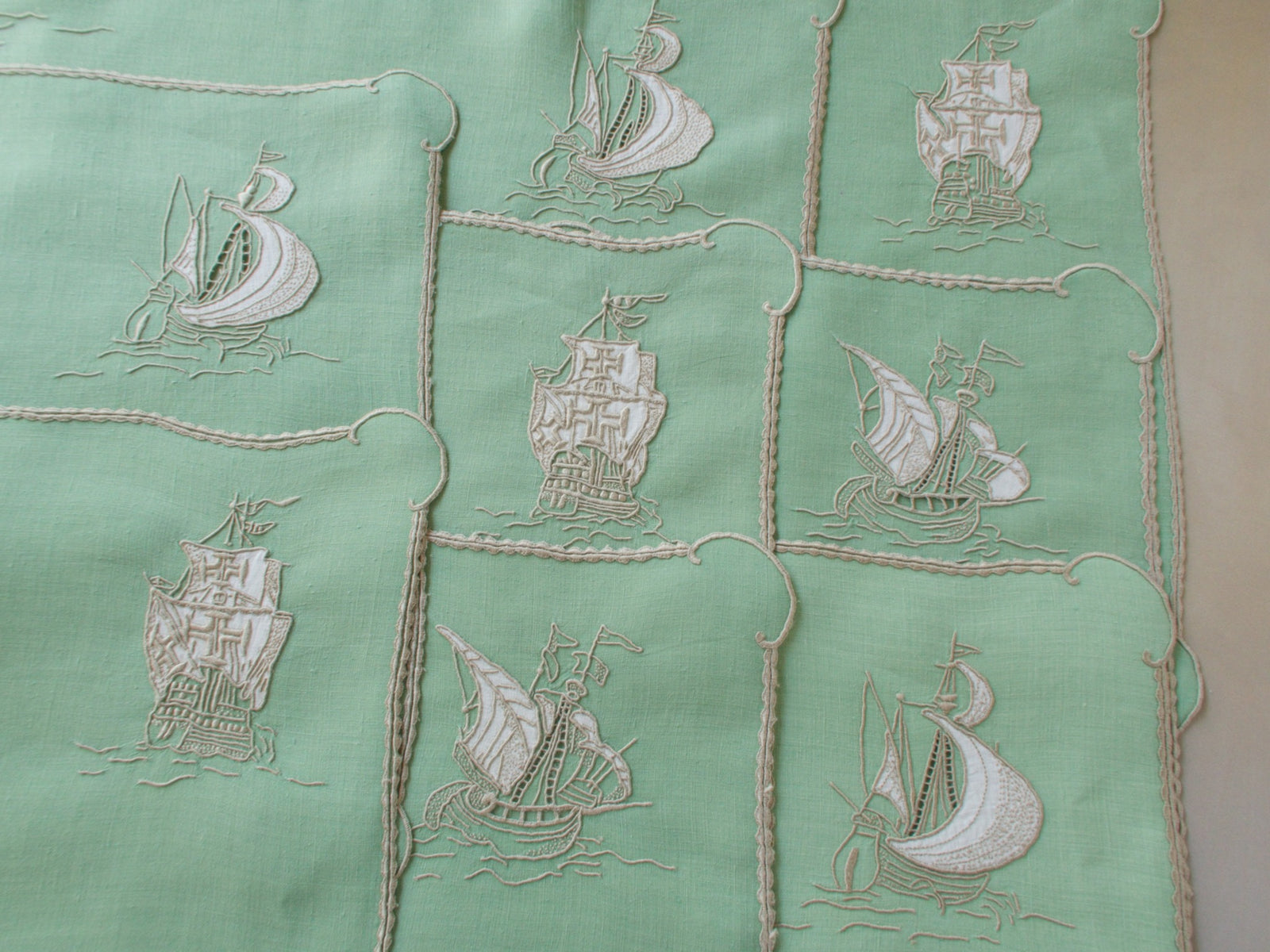 Vintage Marghab “Old Ships” placemat and napkin set, hand embroidered in Madeira on fine Irish linen in sea-green tones, featuring ships, waves, and mythical sea creatures in intricate raised embroidery.