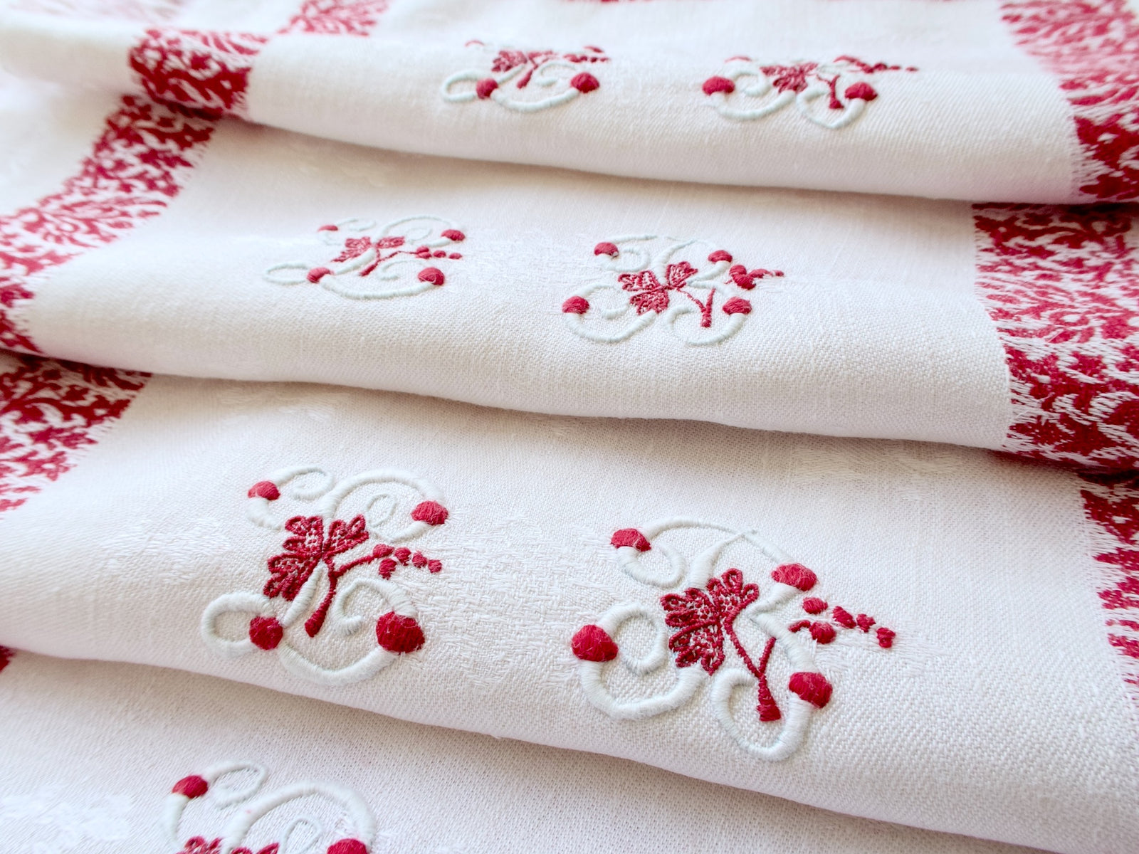 Folded napkins showing the embroidered LB monograms with red leaves and grapes.
