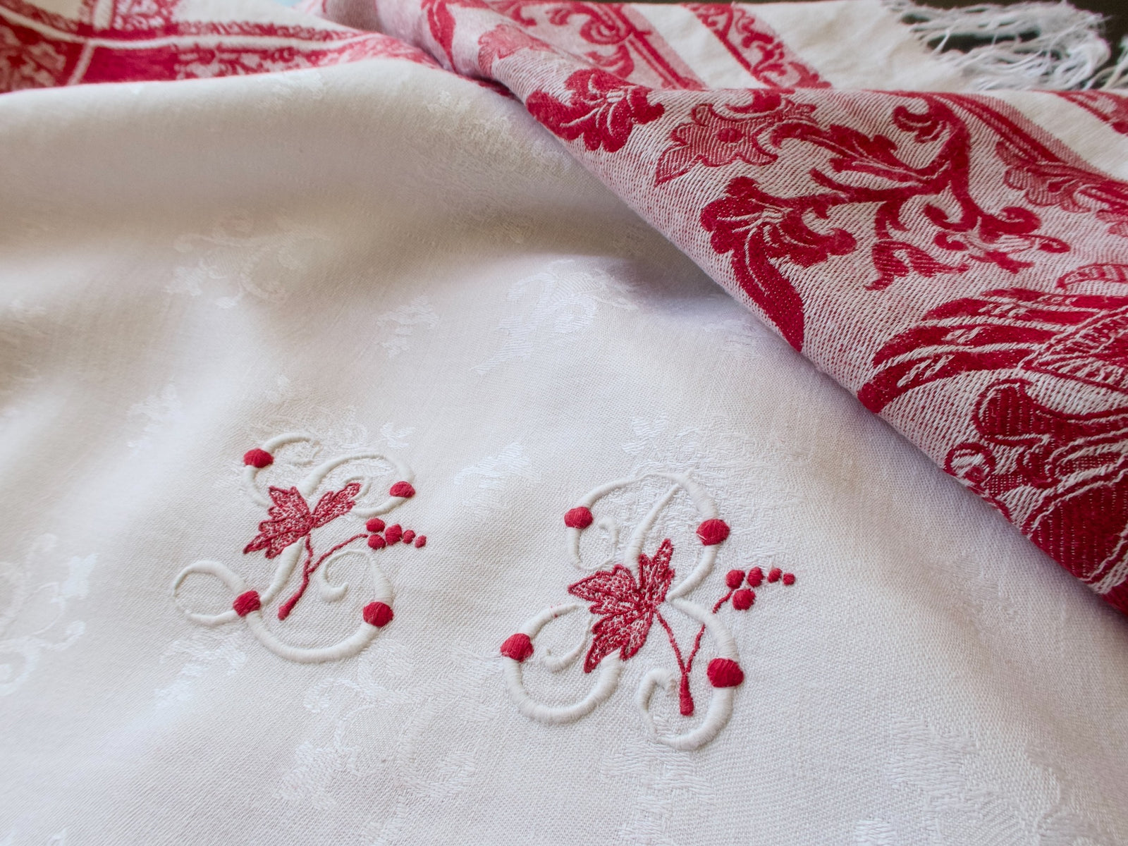 Close-up of an LB monogram embroidered in raised white and red stitching on the damask.