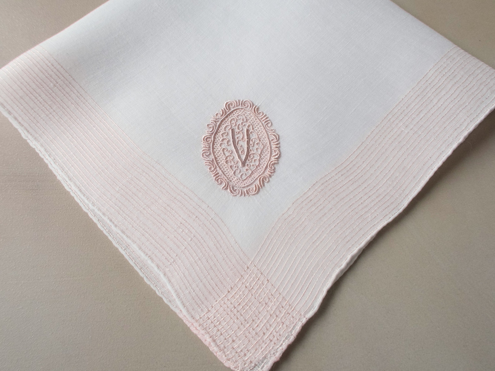 Vintage Marghab handkerchief featuring a “V” monogram in the “Oval Initial” pattern, worked in soft pink embroidery on fine linen. Hand embroidered in Madeira.