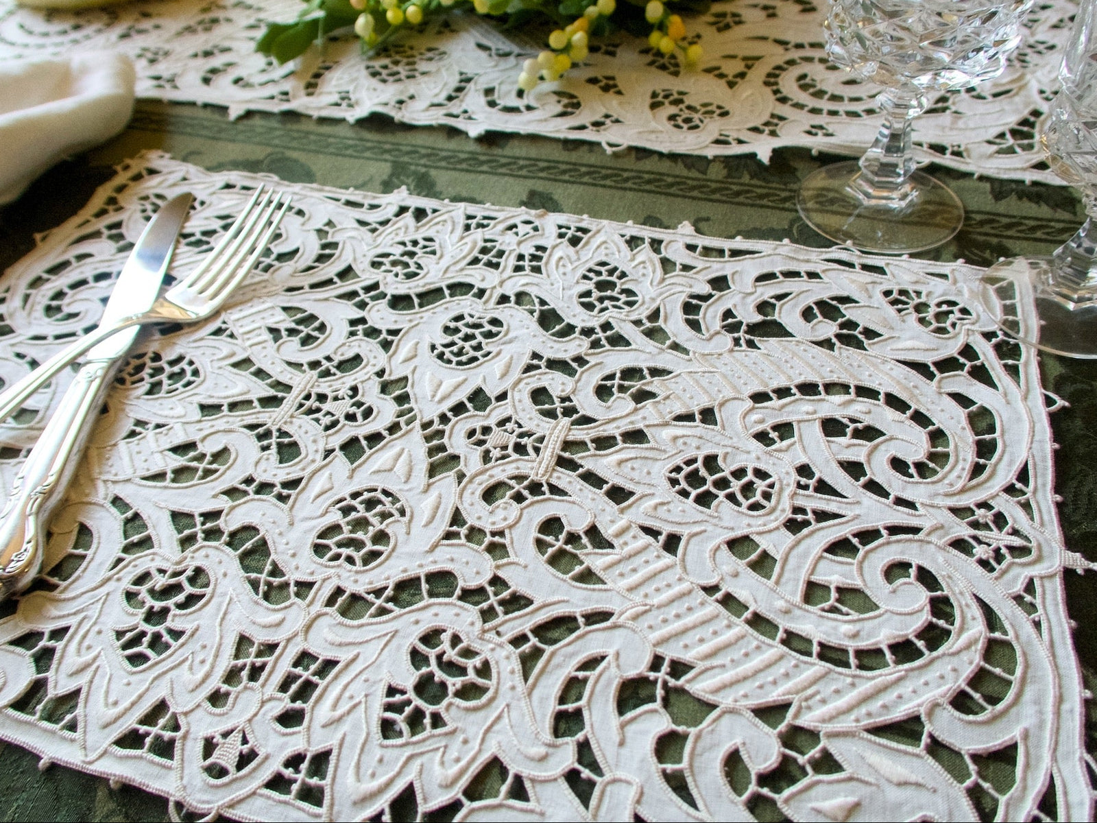 Vintage Italian linen cutwork placemat with bold sculptural embroidery, styled on a green table setting with silver flatware and crystal.