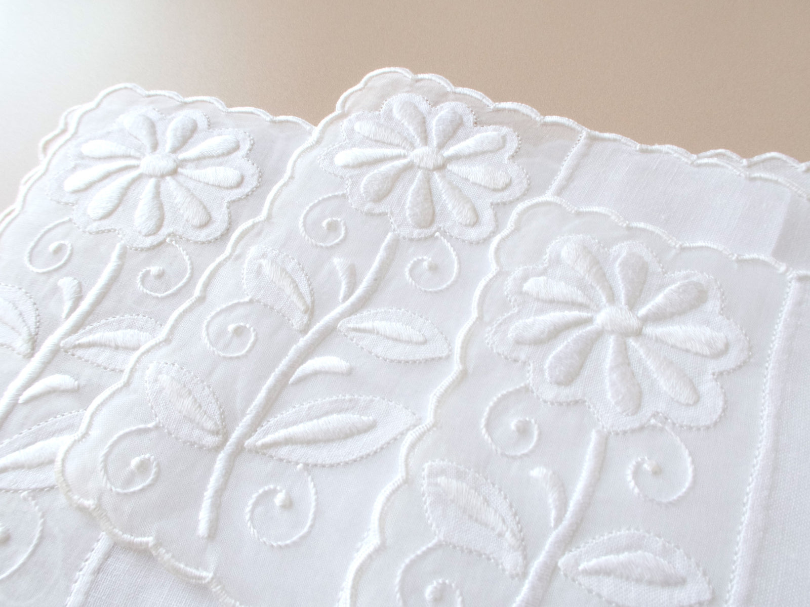 Close detail of vintage Madeira white appliqué cocktail napkins showing heavily padded daisy embroidery with stems, leaves and scalloped edge.