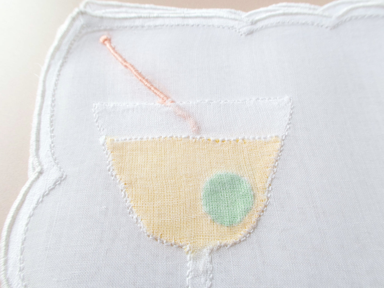 Close-up of vintage Madeira organdy cocktail napkin martini glass with sheer organdy olive overlay and embroidered cocktail pick detail.