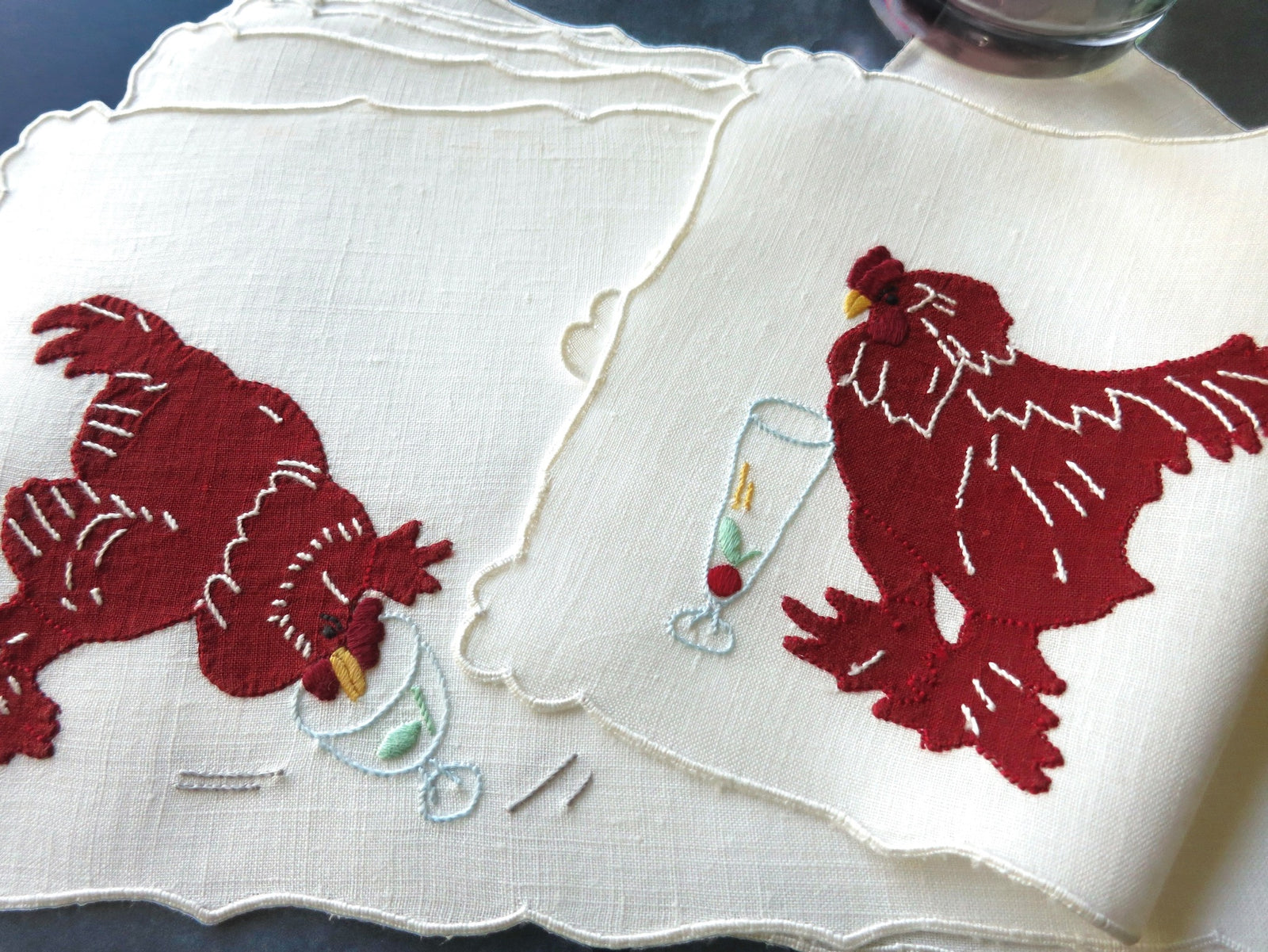 Vintage Madeira linen cocktail napkins showing red appliqué roosters pecking at garnishes with one rooster beside a tall champagne flute on linen