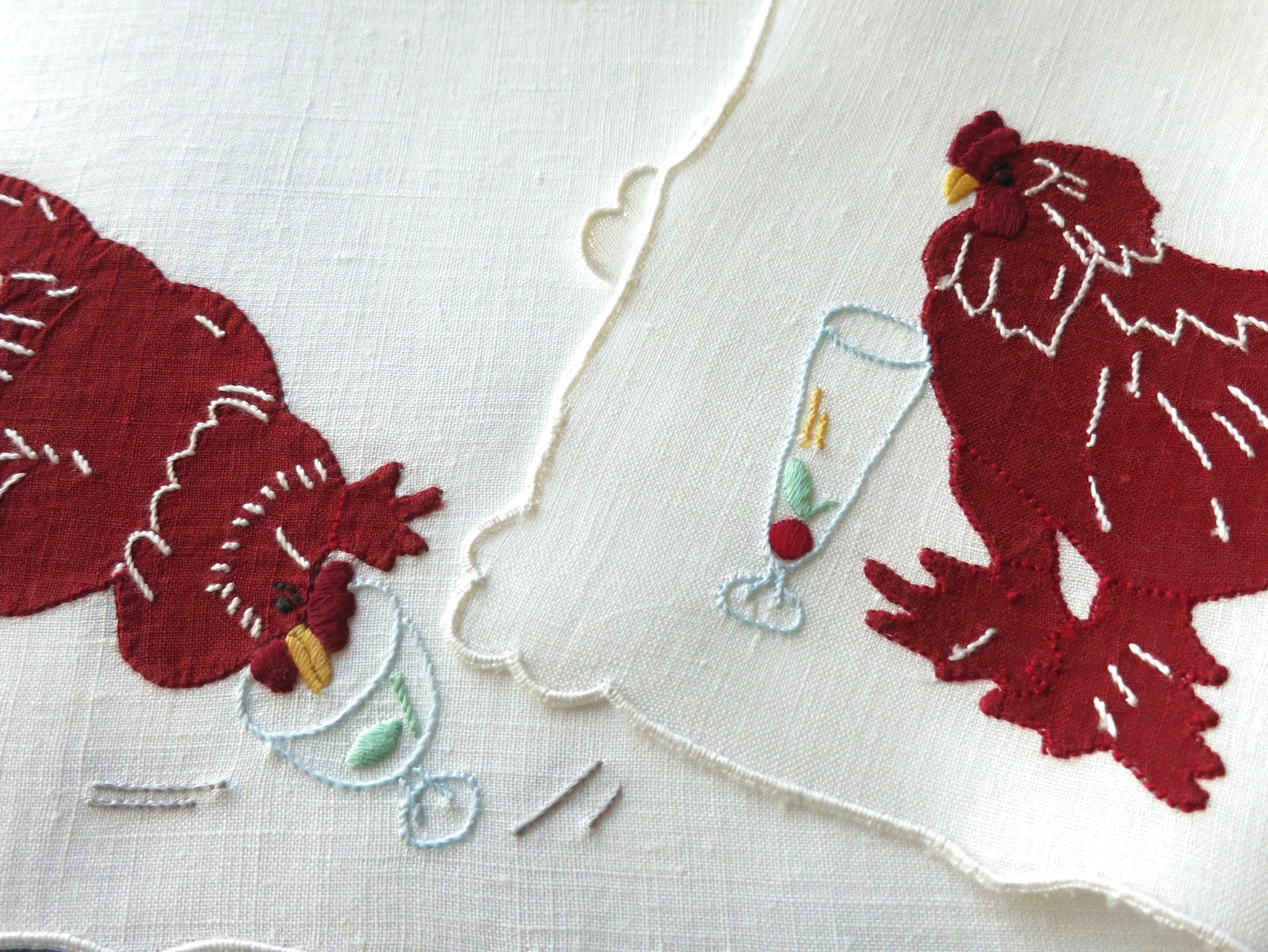 Vintage Madeira linen cocktail napkins showing red appliqué roosters pecking at garnishes with one rooster beside a tall champagne flute on linen