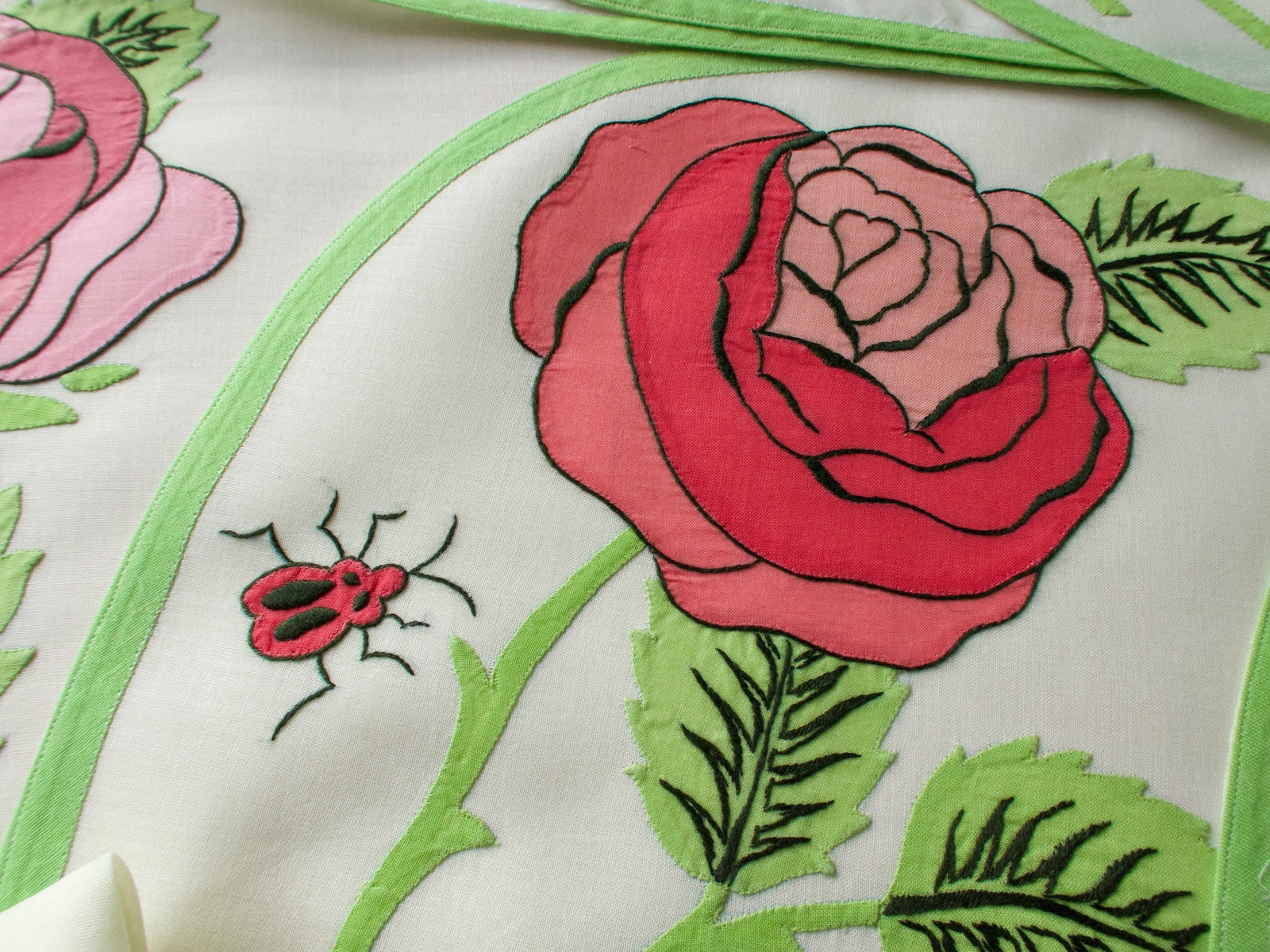 Close-up of vintage Italian appliqué placemat featuring bold red rose and ladybug on semi-sheer linen with green border