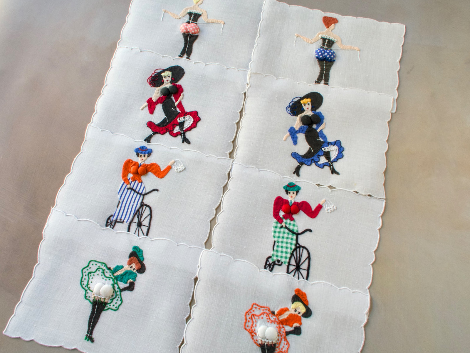 Vintage Madeira Paragon cocktail napkins showing colorful hand-embroidered ladies — cyclists, dancers, and flirts — with padded appliqué details.