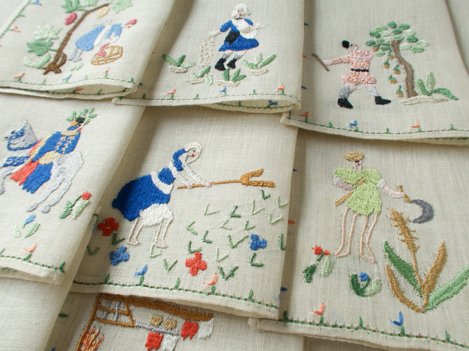 Close-up of three embroidered monthly scenes including August, September, and November, with figures in motion and scattered florals.