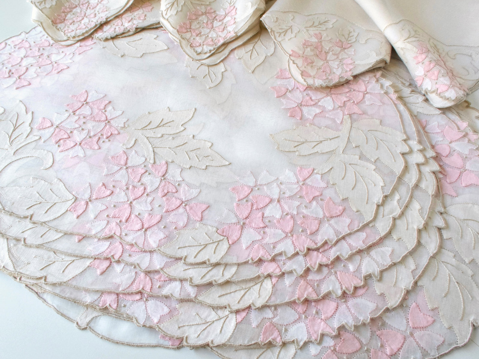 Stack of vintage Madeira pink viburnum organdy placemats showing set of 8 with consistent appliqué design and scalloped edges.