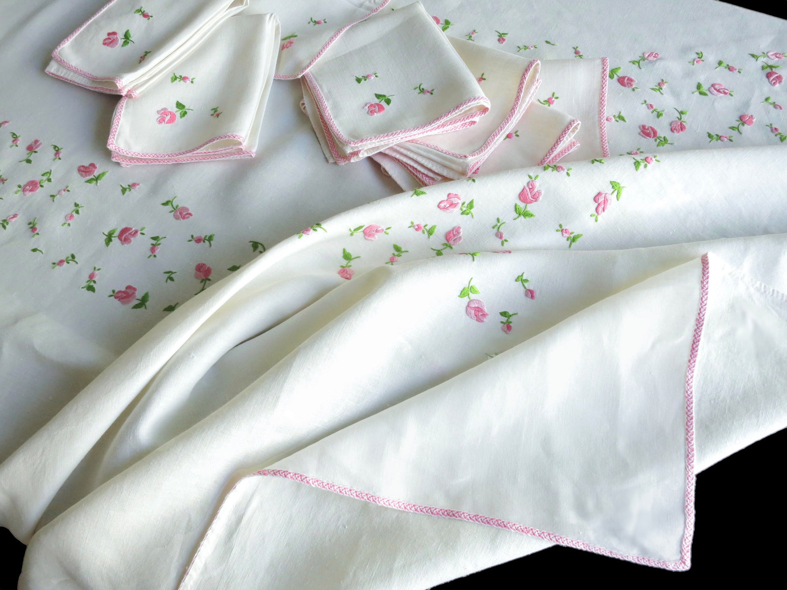 Stack of vintage European linen napkins hand embroidered with scattered rosebuds and pale pink monogram, showing continental sizing
