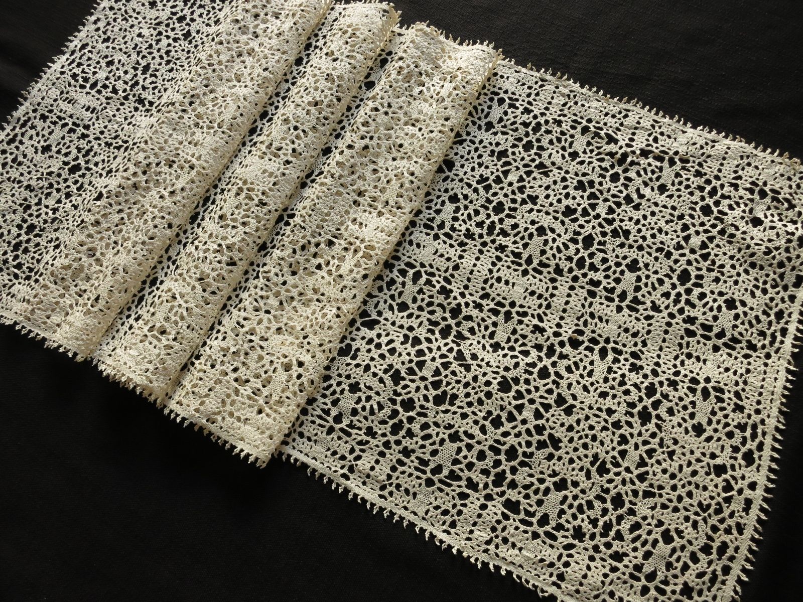 Antique ecru bobbin lace table runner folded, showing length and consistent pattern throughout.