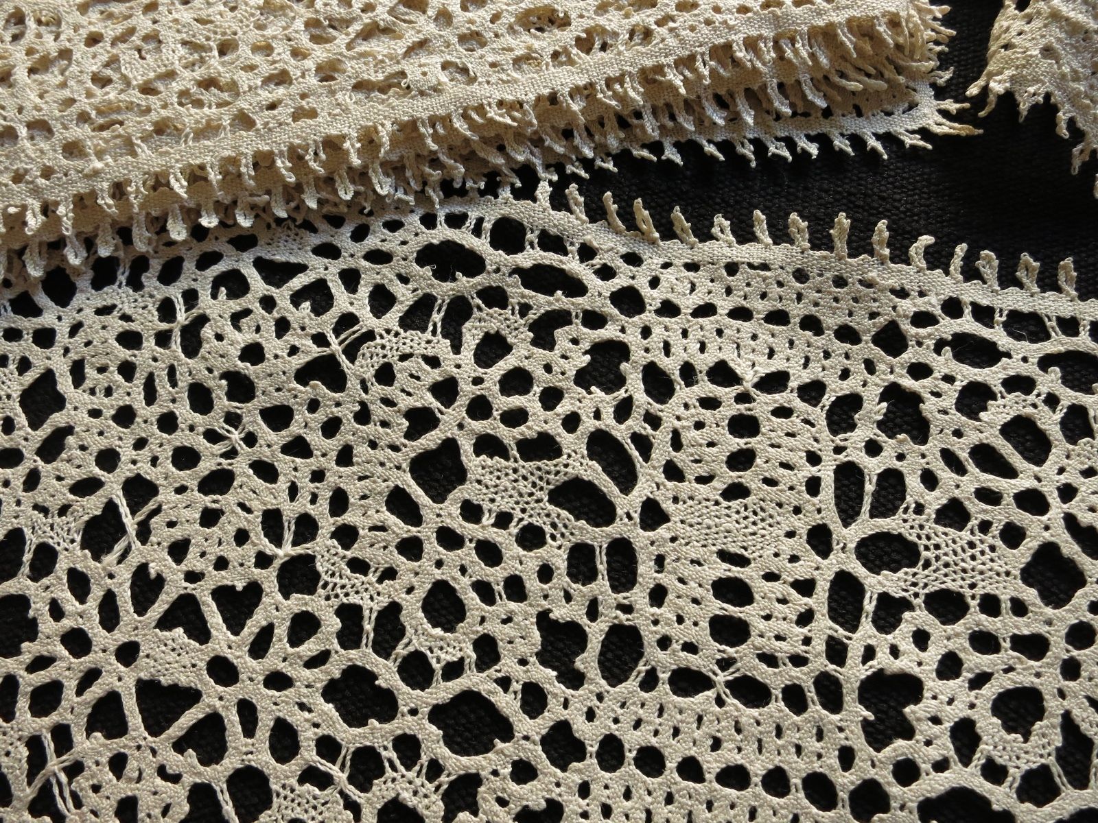 Close-up of antique ecru bobbin lace placemat showing flowing organic pattern and picot edging detail against dark background.
