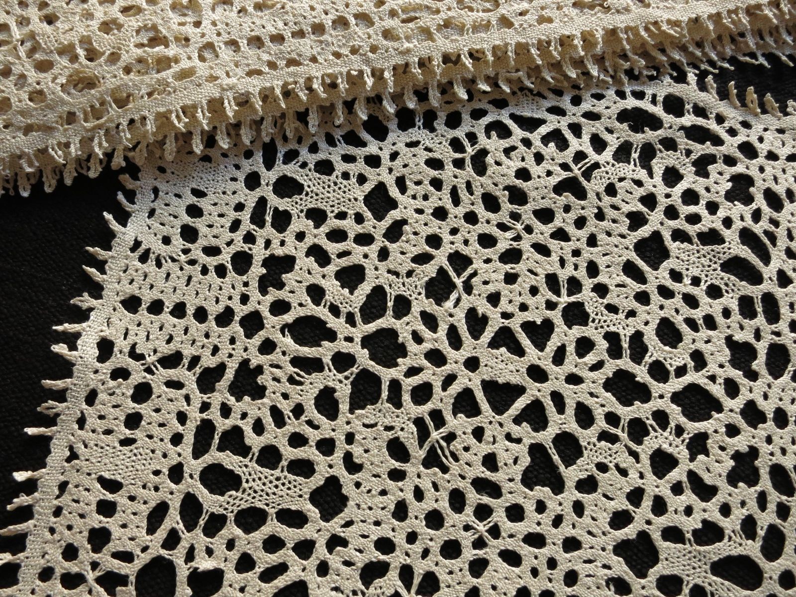 Detail view of antique ecru bobbin lace showing open organic pattern structure and handmade construction.