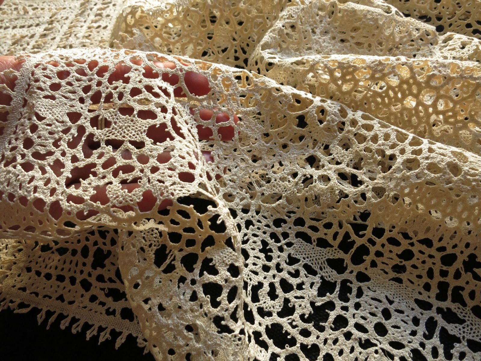 Antique ecru bobbin lace pieces layered together, showing scale and the supple, airy quality of the fabric.
