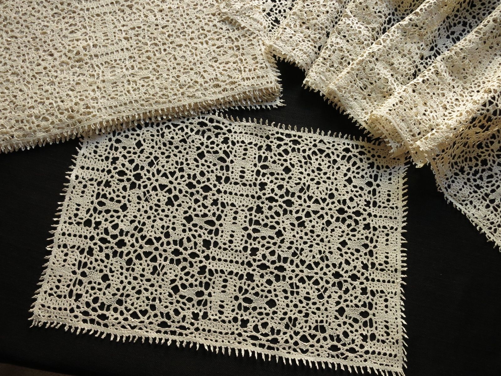 Antique ecru bobbin lace placemats stacked and folded, showing texture and depth of the lacework.