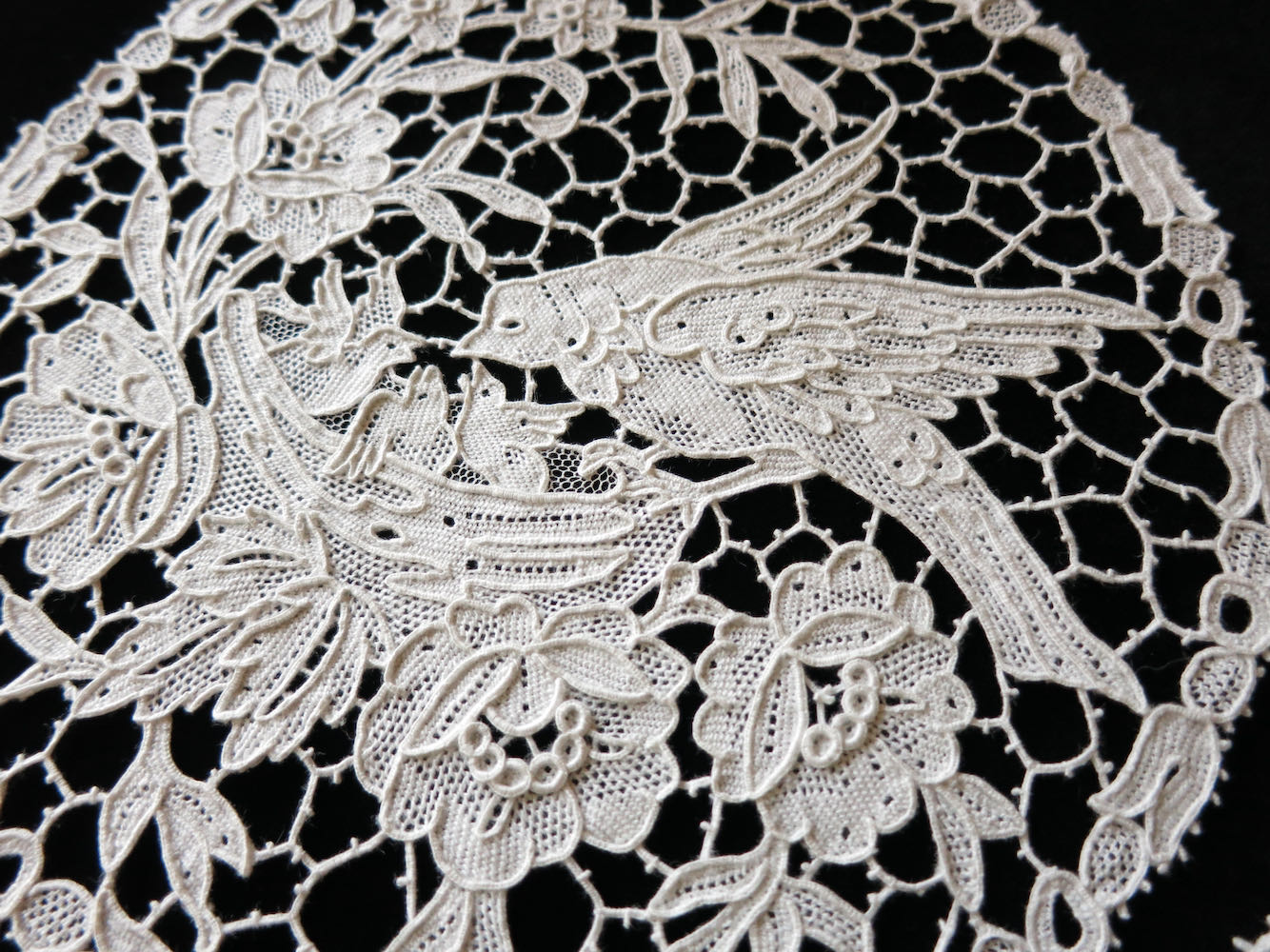 Antique Italian needle lace with a bird feeding its young, surrounded by detailed flowers and foliage.