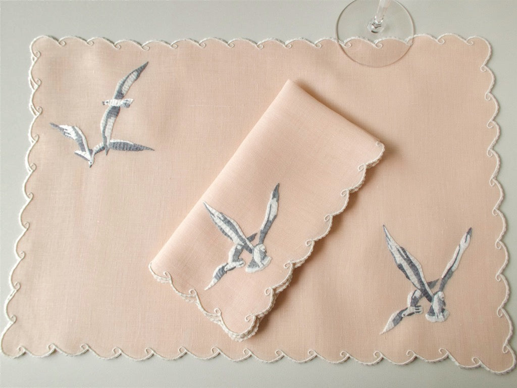 Vintage Madeira coral linen place setting with folded napkin, showing seagull embroidery and caseado bastido wave border.