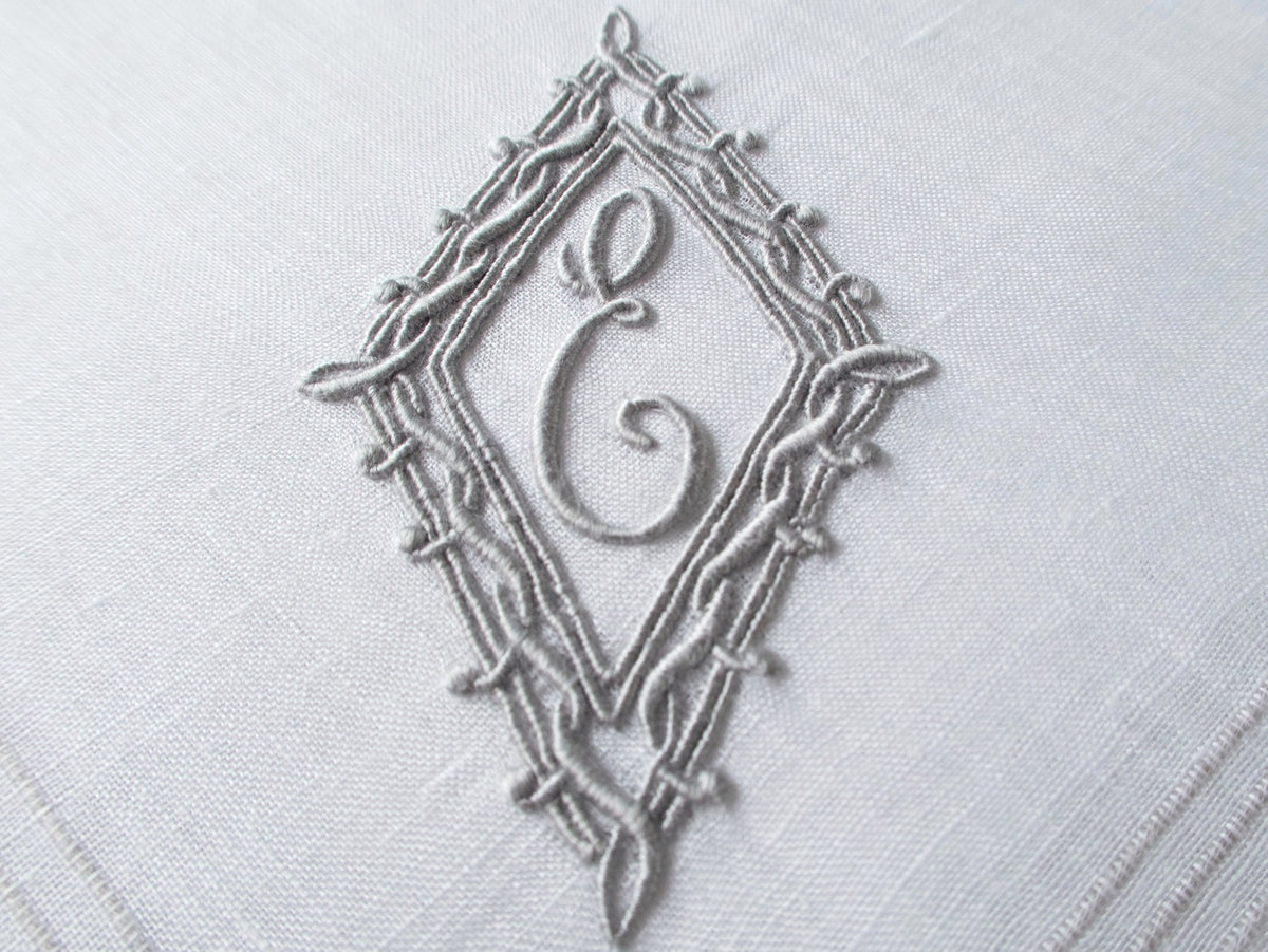 Vintage Marghab handkerchief featuring an “E” monogram framed in twisted cord and bordered by the “Hand Inserted Threads” pattern. Hand embroidered in Madeira on fine linen.