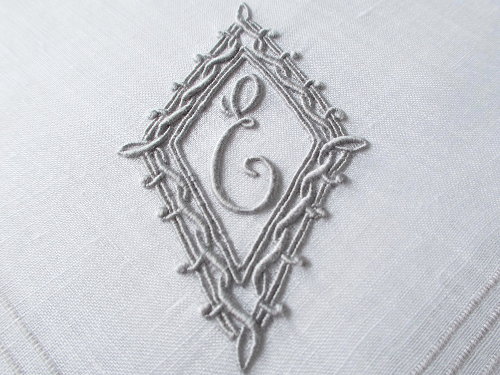 Vintage Marghab handkerchief featuring an “E” monogram framed in twisted cord and bordered by the “Hand Inserted Threads” pattern. Hand embroidered in Madeira on fine linen.