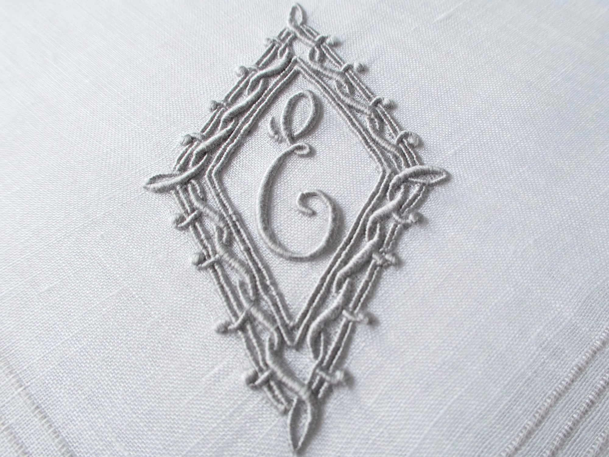 Vintage Marghab handkerchief featuring an “E” monogram framed in twisted cord and bordered by the “Hand Inserted Threads” pattern. Hand embroidered in Madeira on fine linen.