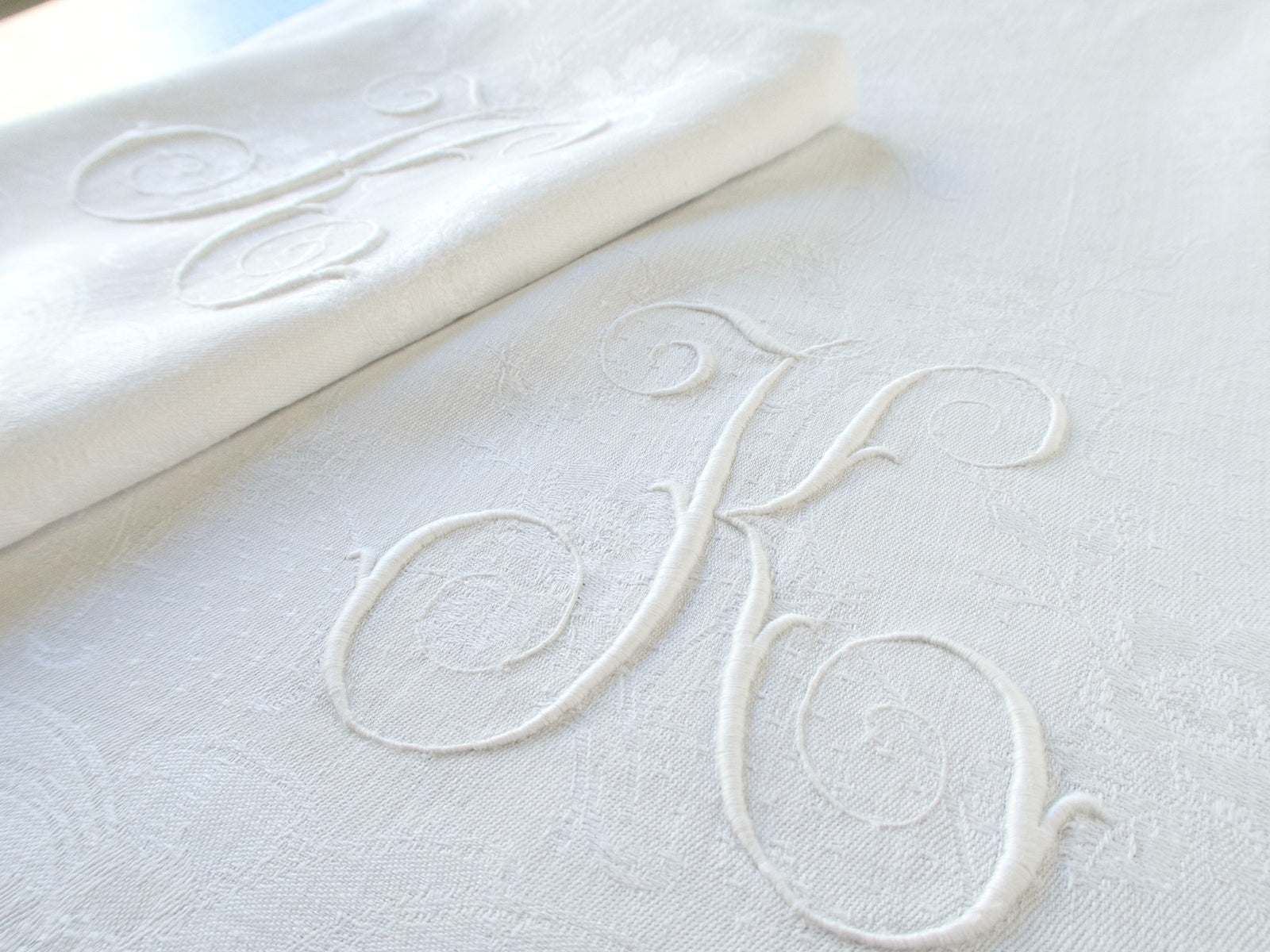 Close-up of a raised white-on-white embroidered monogram on a damask linen napkin.