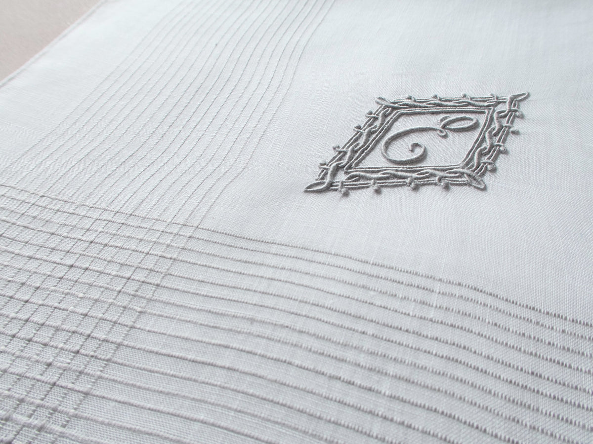 Vintage Marghab handkerchief featuring an “E” monogram framed in twisted cord and bordered by the “Hand Inserted Threads” pattern. Hand embroidered in Madeira on fine linen.