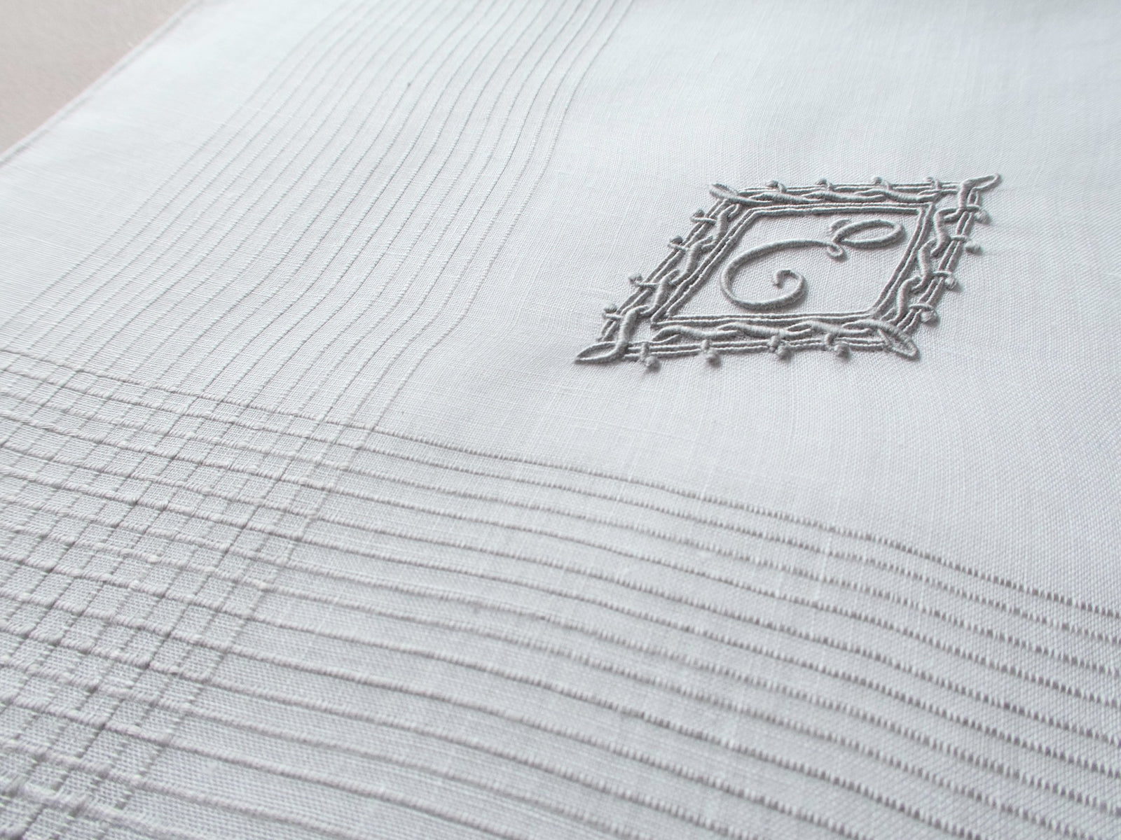 Vintage Marghab handkerchief featuring an “E” monogram framed in twisted cord and bordered by the “Hand Inserted Threads” pattern. Hand embroidered in Madeira on fine linen.