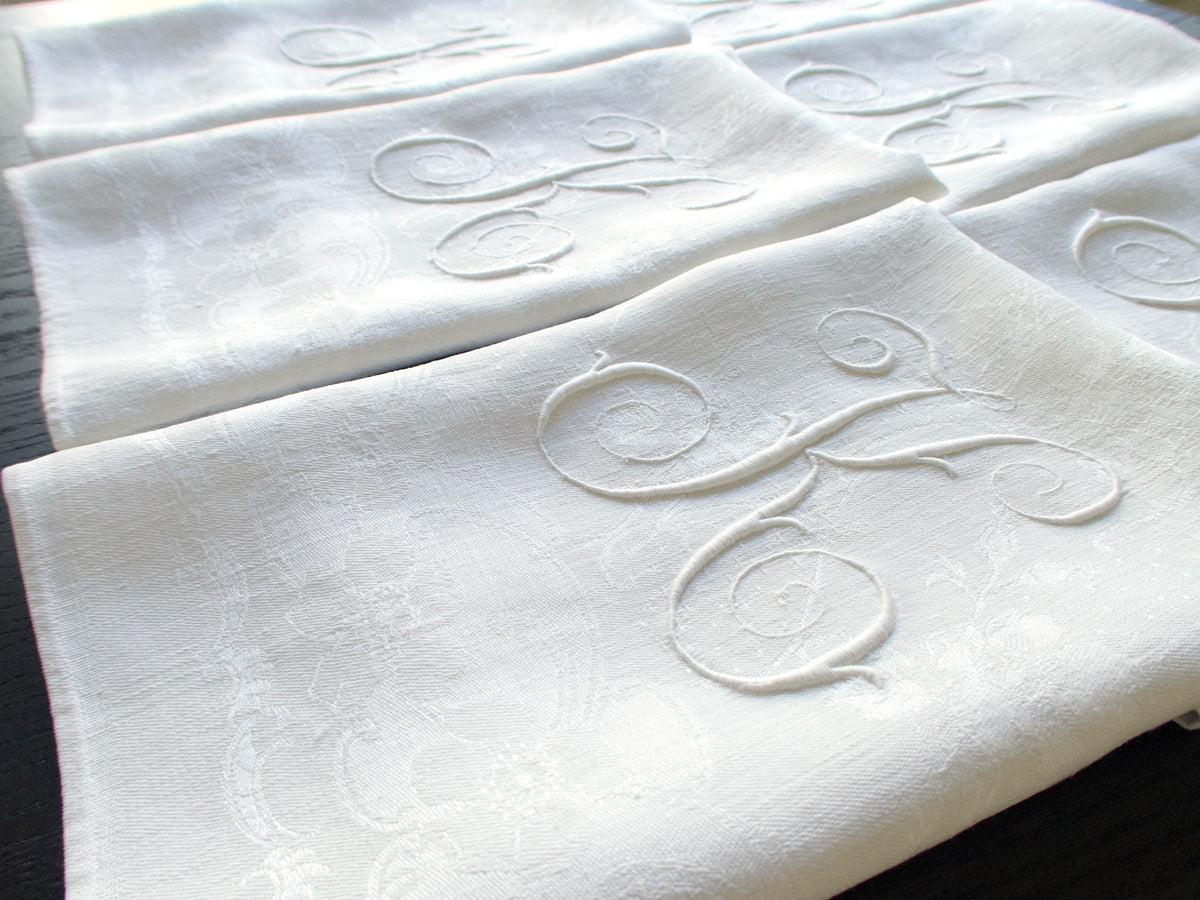     Angled close-up of several damask linen napkins with sweeping white-on-white monograms.