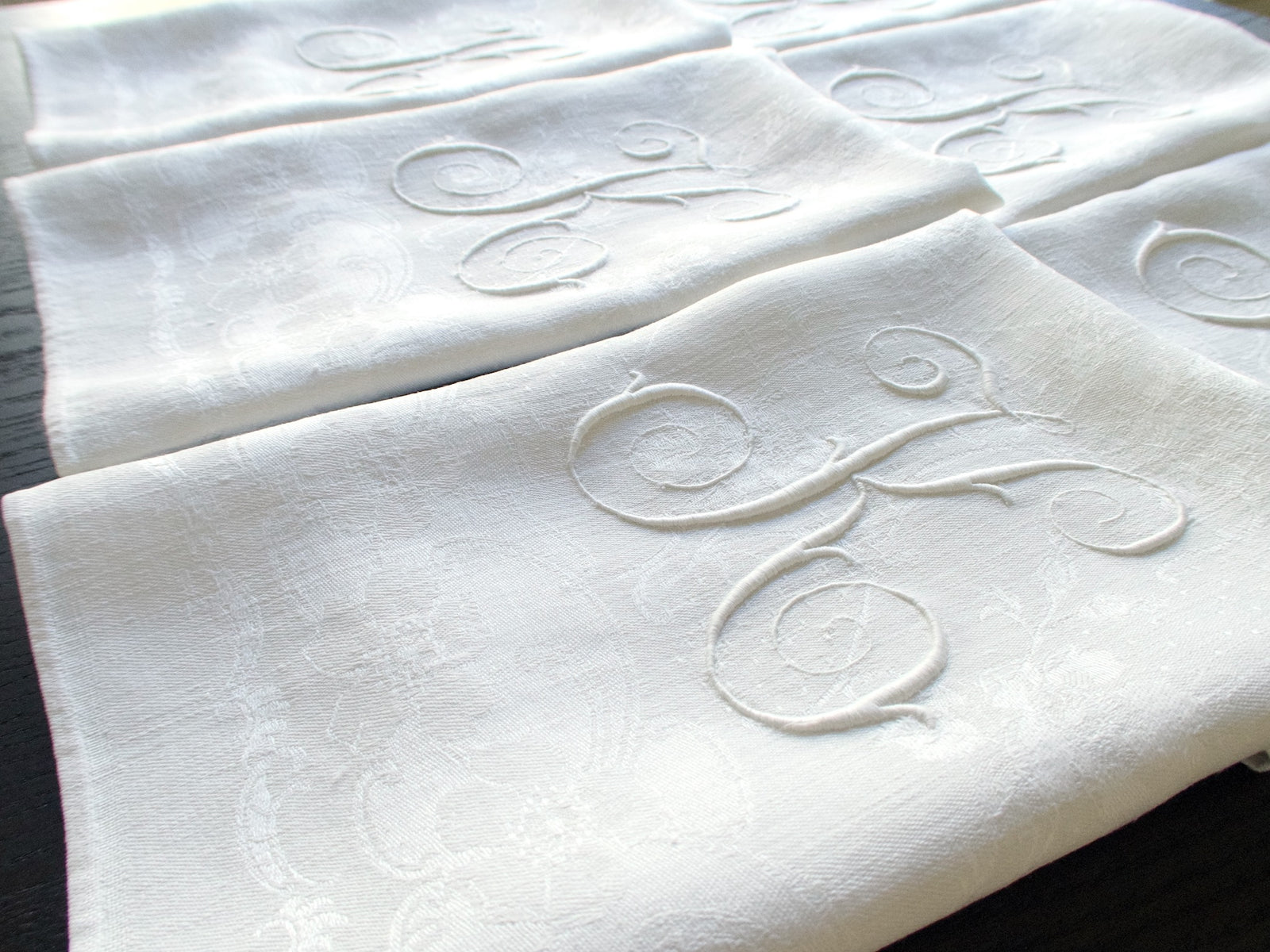     Angled close-up of several damask linen napkins with sweeping white-on-white monograms.