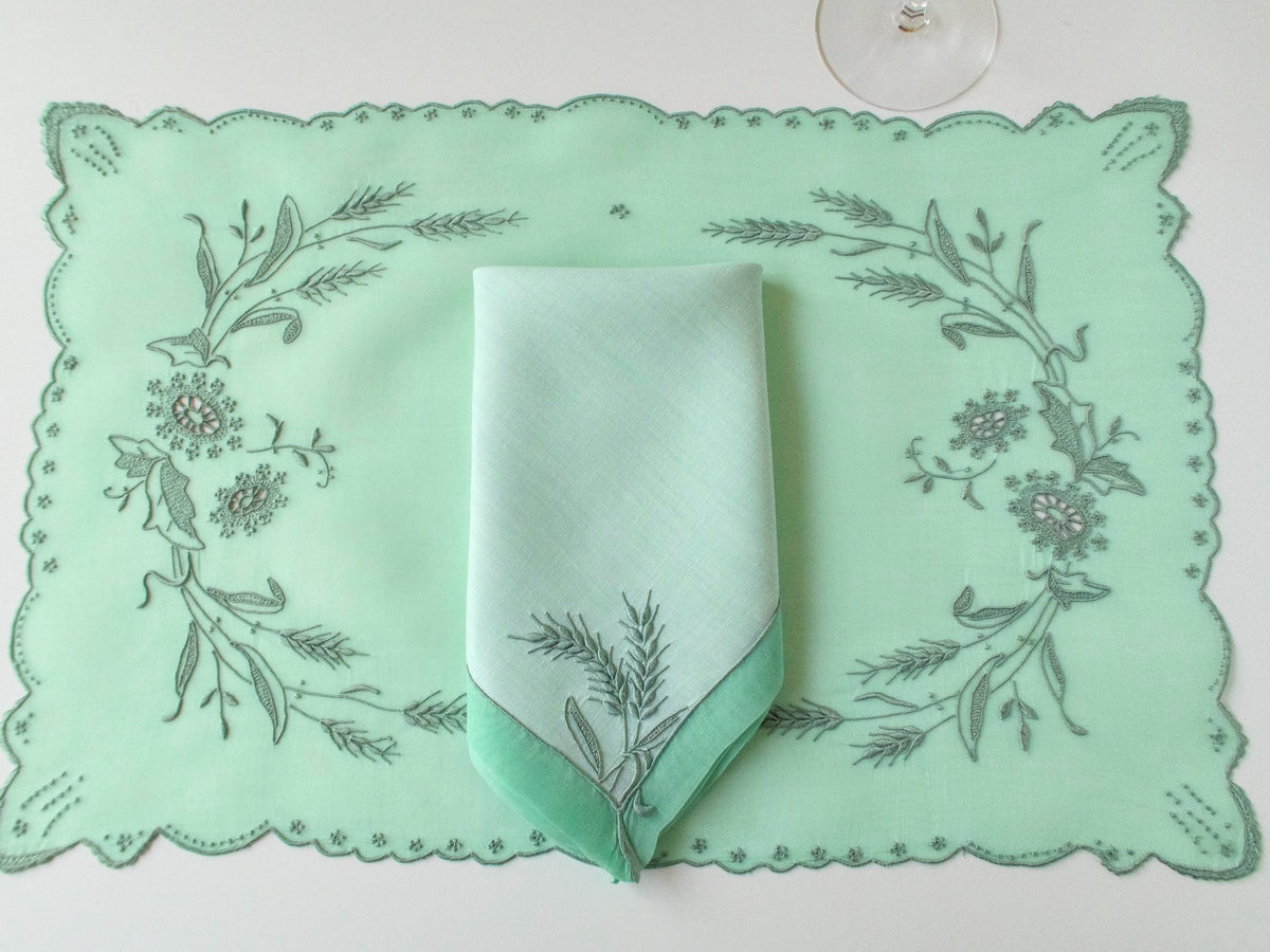 Green Marghab Wheat placemat laid flat with a folded napkin at its center, showing the embroidered design and scalloped border.